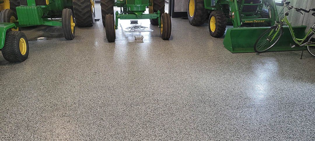 Row of green tractors and lawn mowers displayed on a speckled showroom floor.