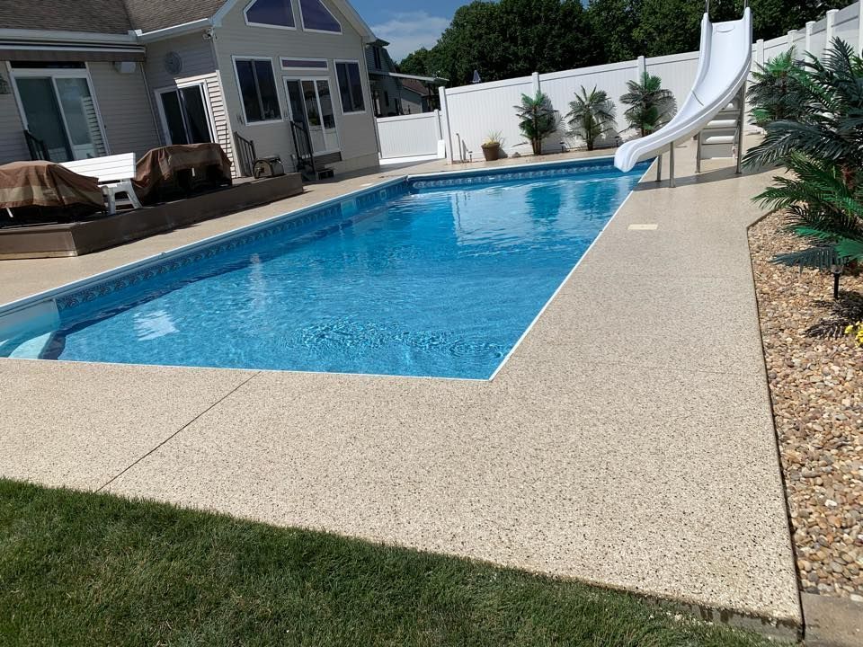 Backyard swimming pool with a slide, patio, and house under a bright sky