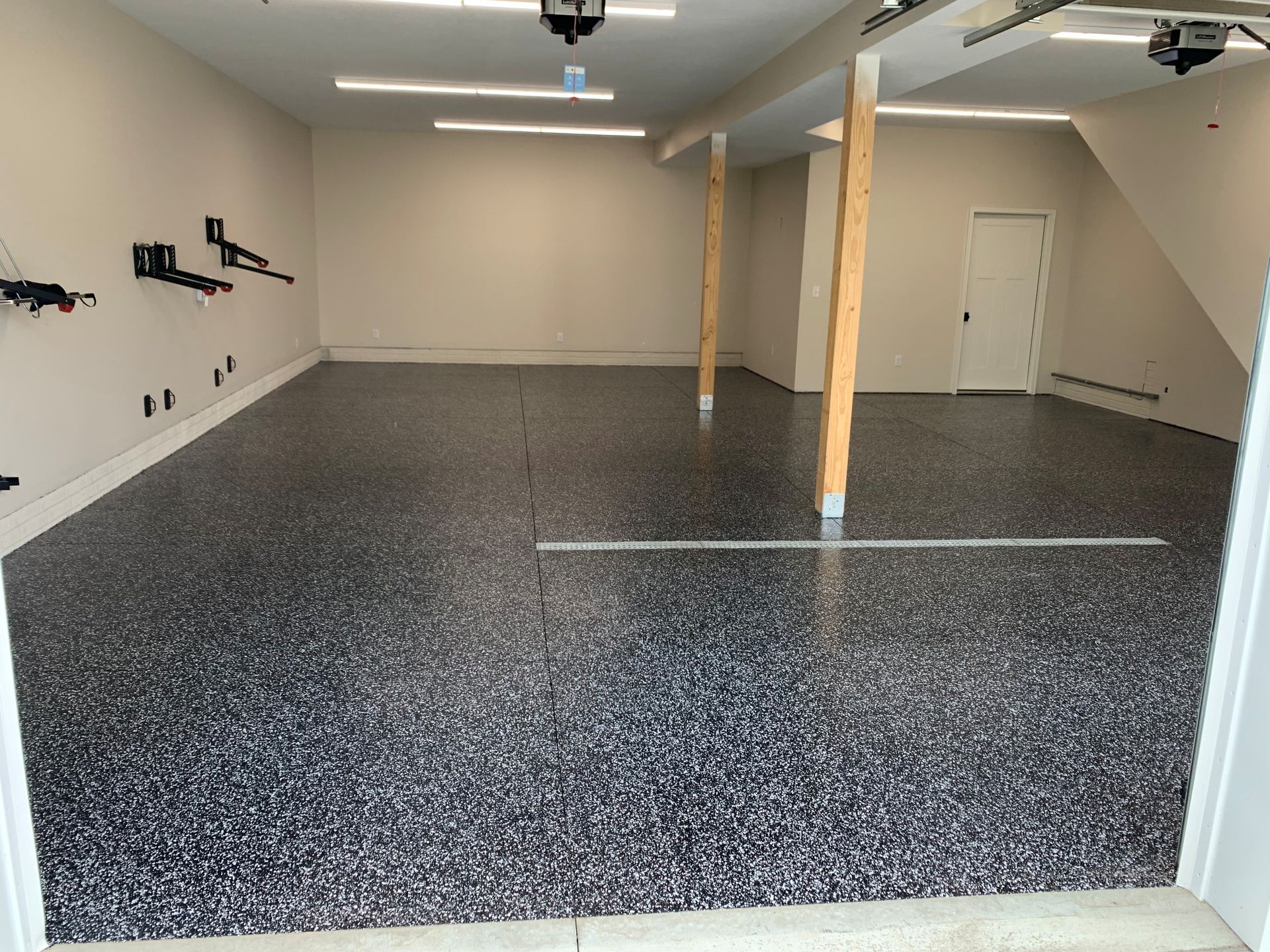 Empty garage with speckled epoxy floor, ceiling lights, and wooden support posts