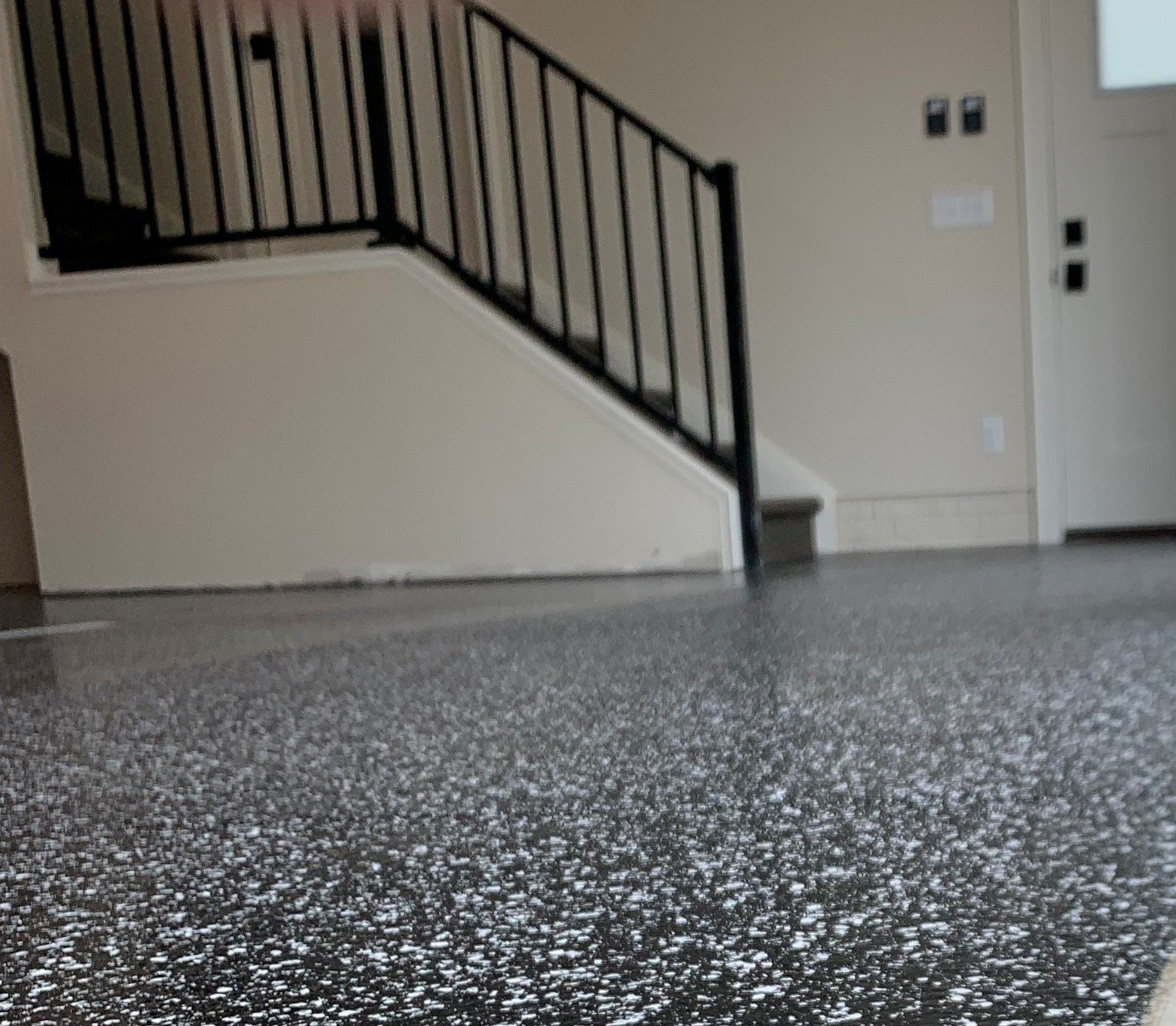 Empty room with speckled floor and a black staircase railing along a beige wall