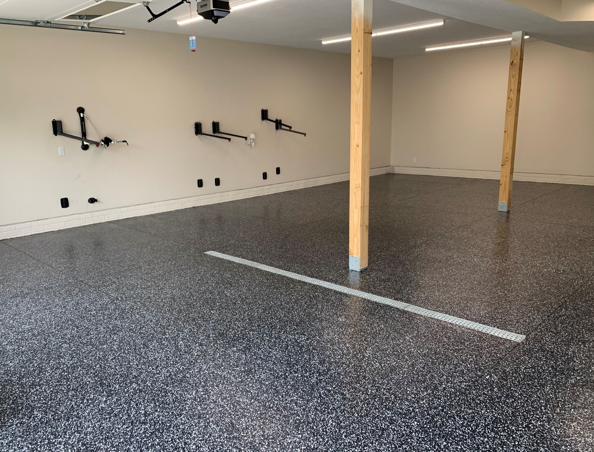 Empty garage with speckled epoxy floor, wall-mounted bike racks, and exposed wooden support posts.
