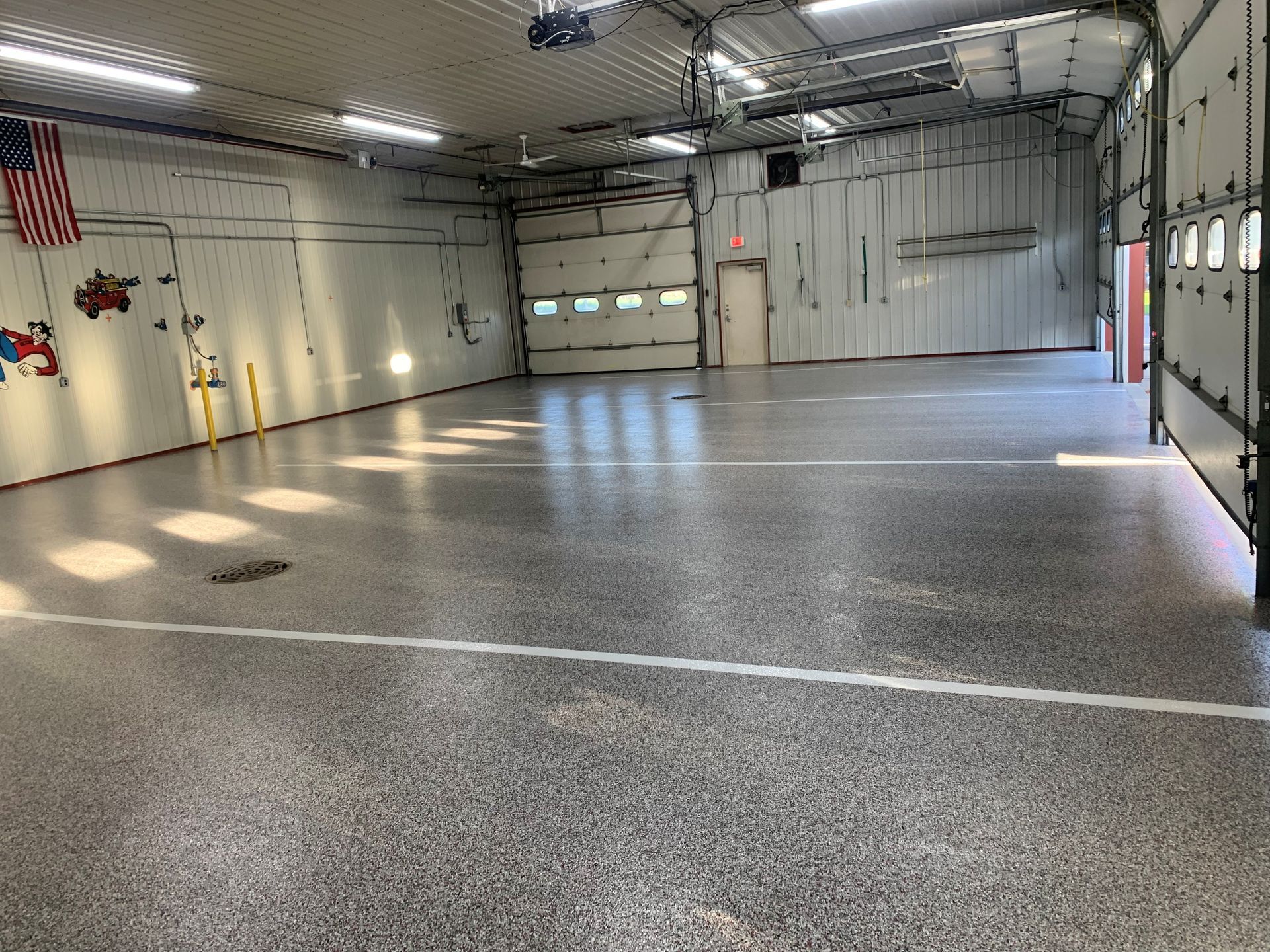 Empty industrial garage with concrete floor, overhead lights, and American flag on the wall