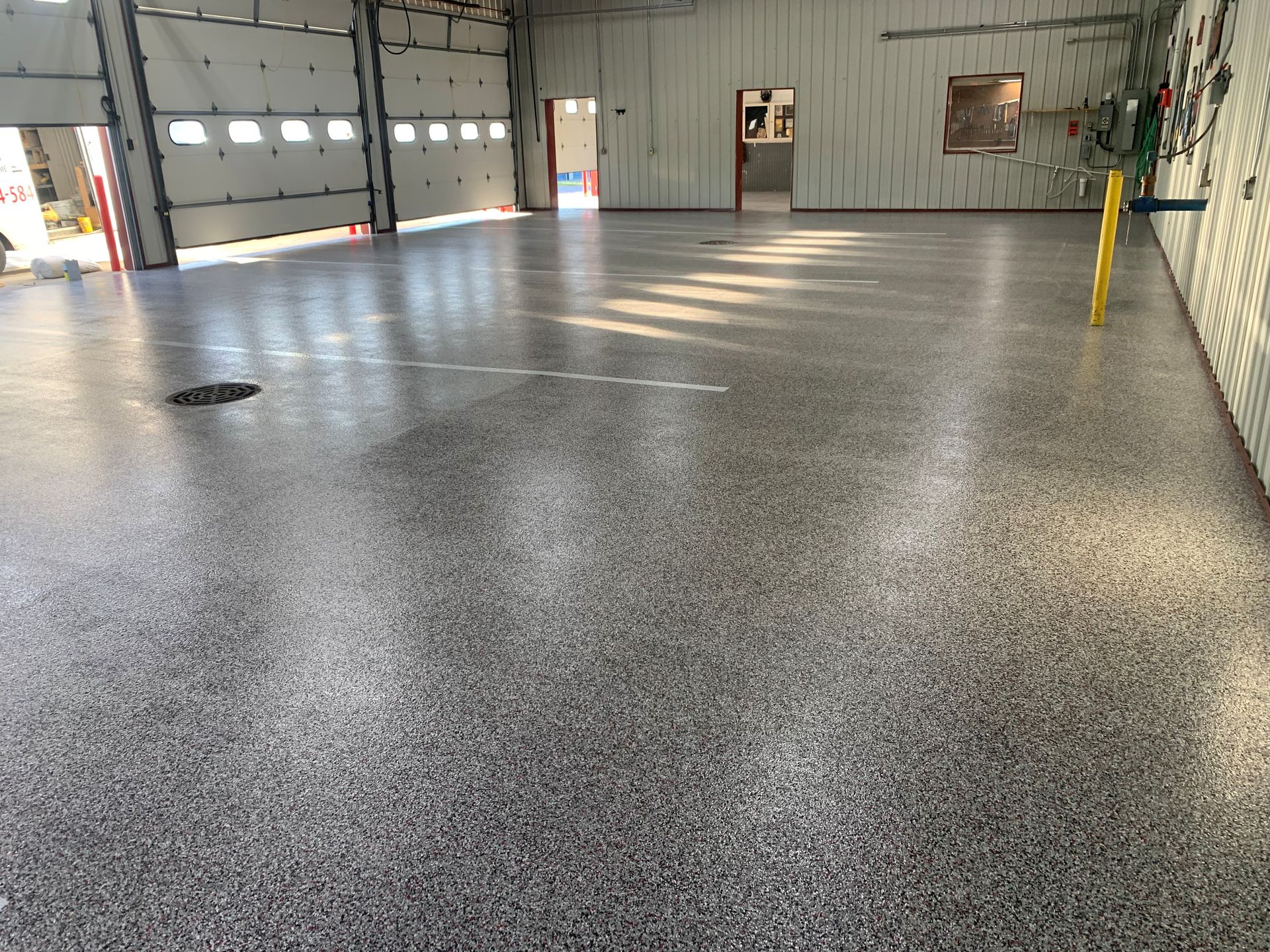 Empty gray-speckled warehouse floor inside a large industrial garage, with garage doors and walls visible.