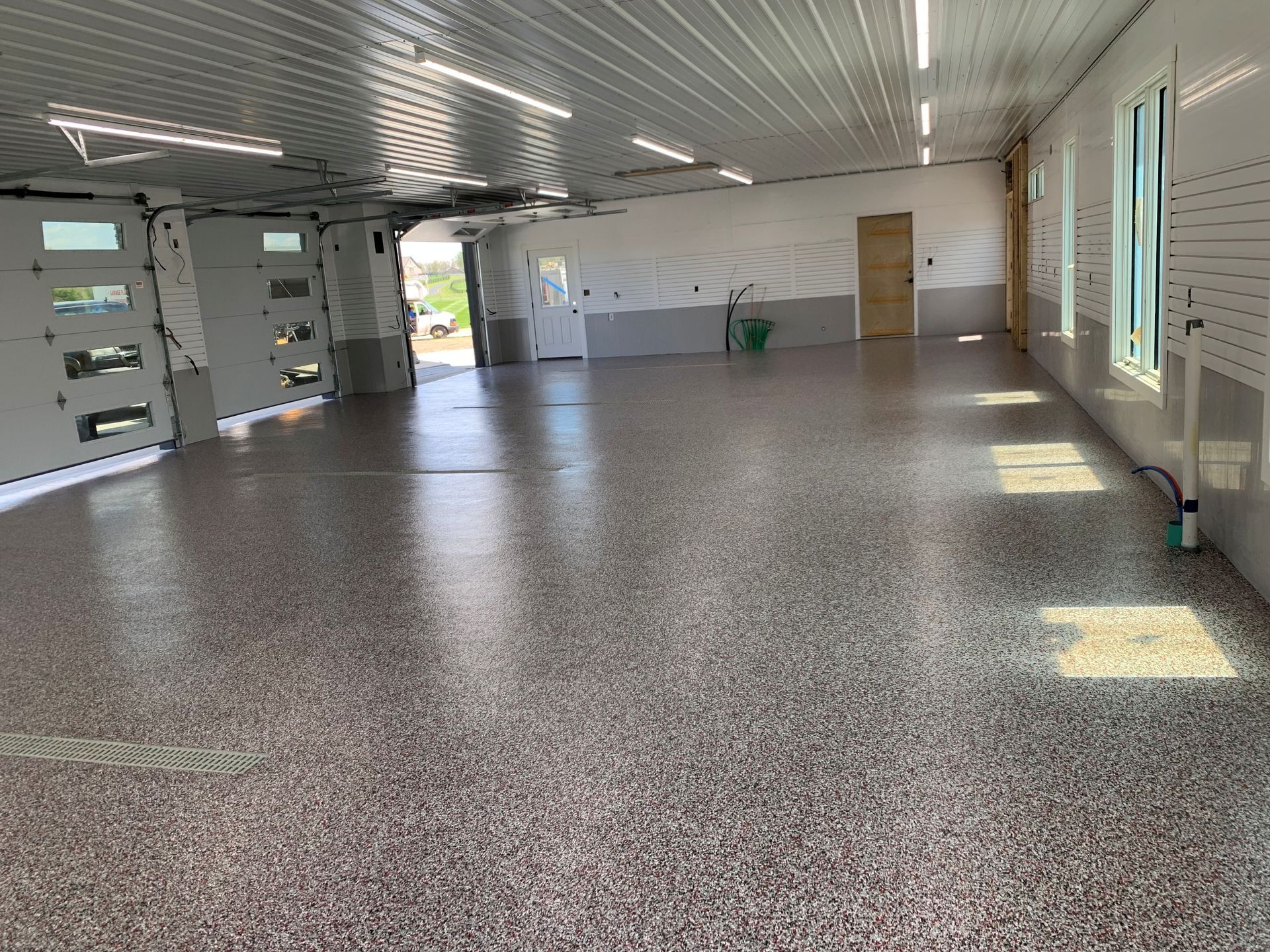 Empty indoor room with terrazzo floor, white walls, and sunlight through windows.