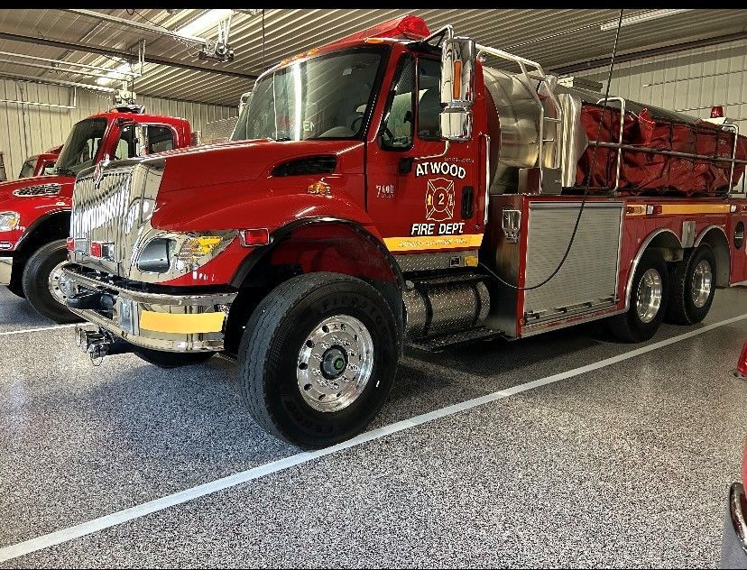 Red fire truck parked indoors on a polished floor, viewed from the front-left side.