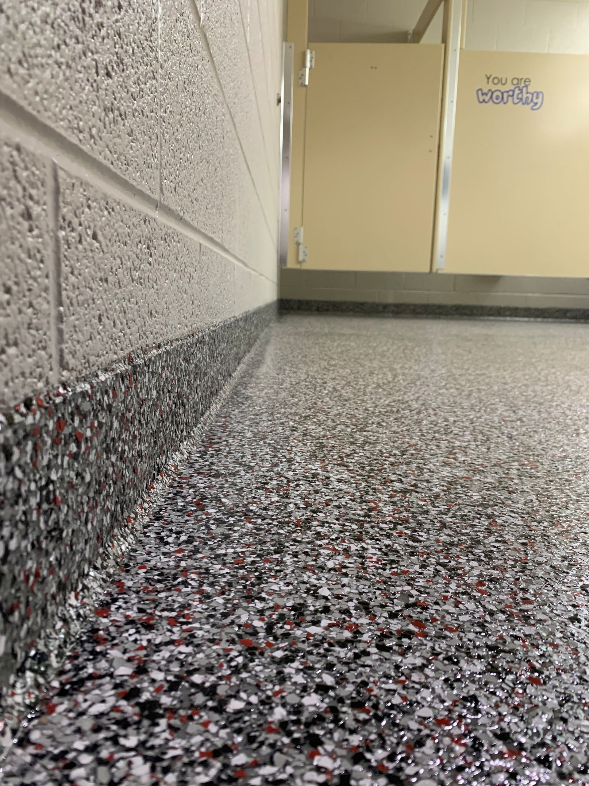 Low-angle view of a speckled hallway floor beside a cinderblock wall and beige cabinets.