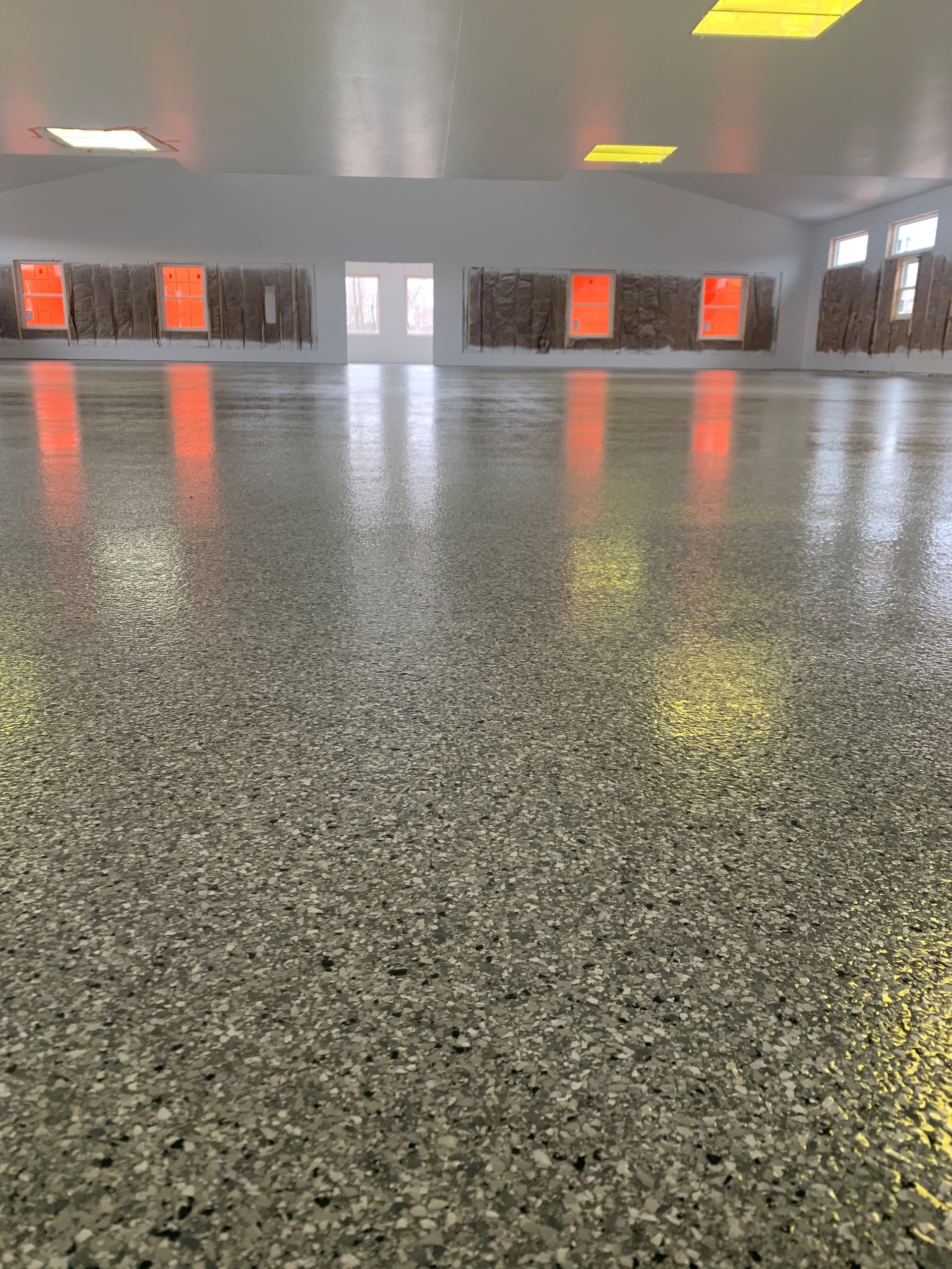 Empty glossy indoor floor with gray walls, orange wall panels, and reflections of ceiling lights