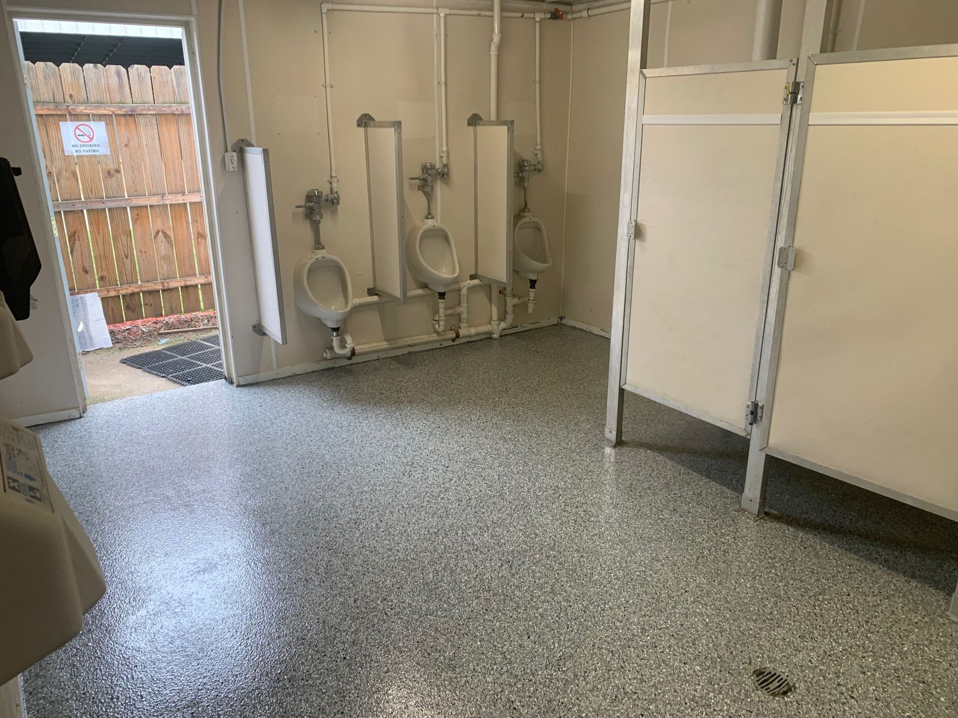 Public restroom with stalls, urinals, and an open door to the outside.