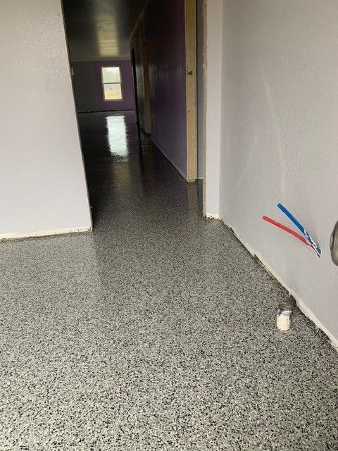 Empty hallway with gray speckled floor and exposed red and blue wires on the right wall