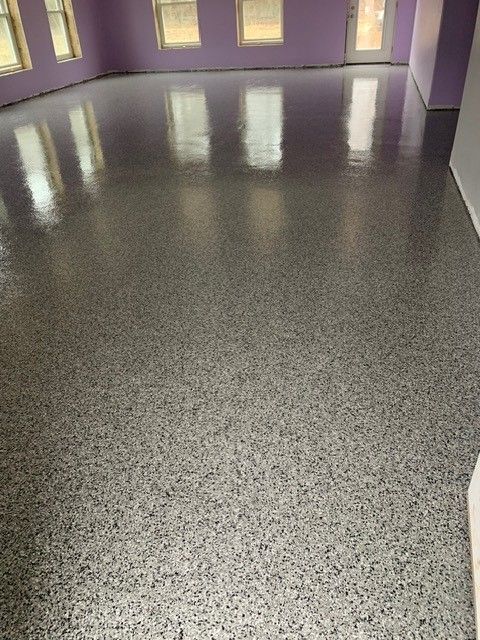 Empty room with glossy dark speckled floor and lavender walls, lit by several windows.