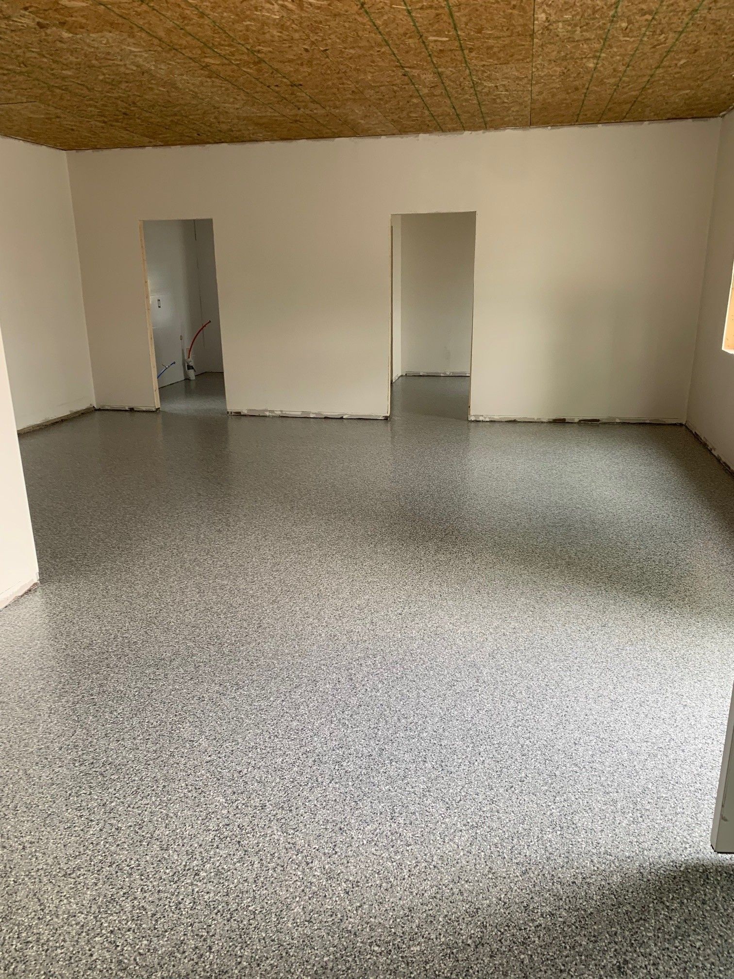 Empty room with speckled floor, beige walls, and two open doorways on the far wall.