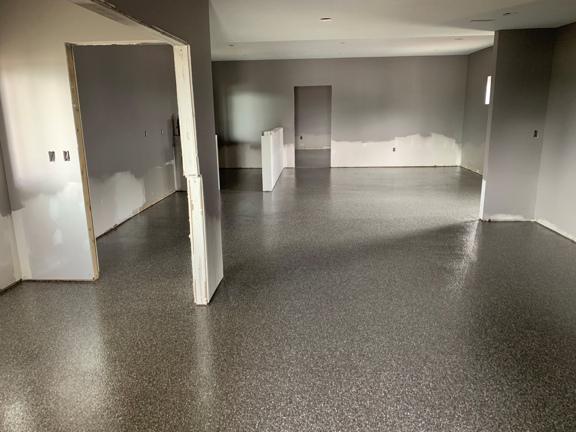 Empty gray room with speckled floor, white walls, and an open doorway.