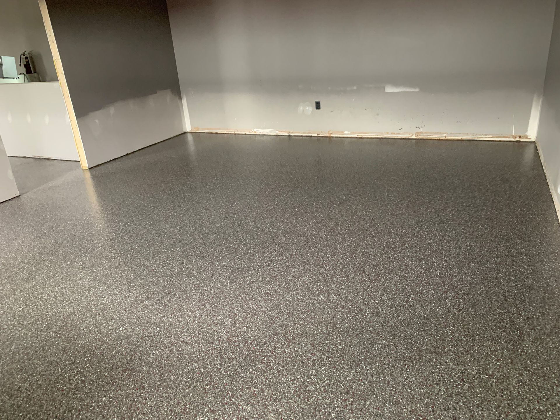 Empty room with gray speckled floor and white walls, viewed from the corner