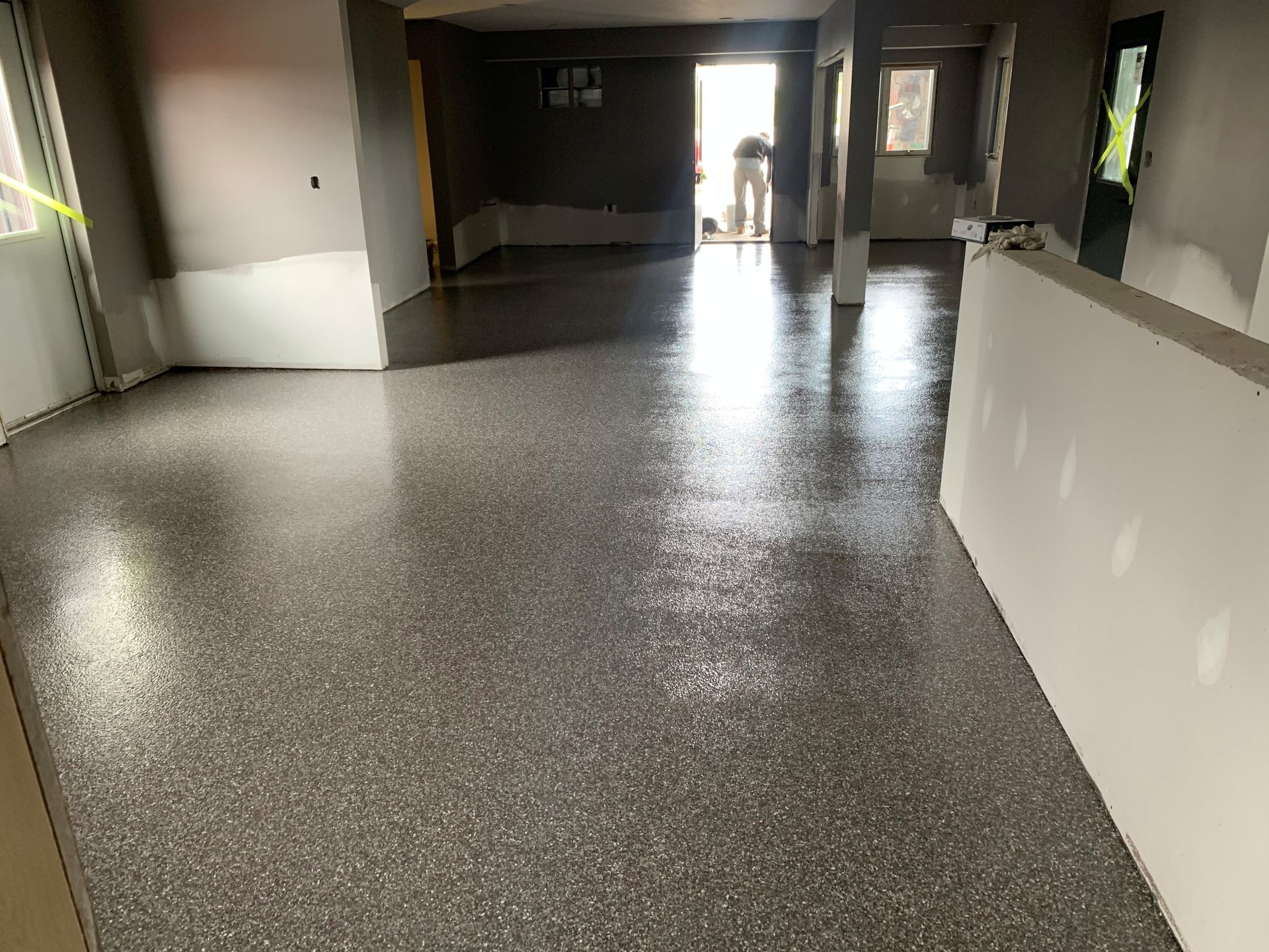 Empty indoor hallway with speckled floor and bright doorway at the end