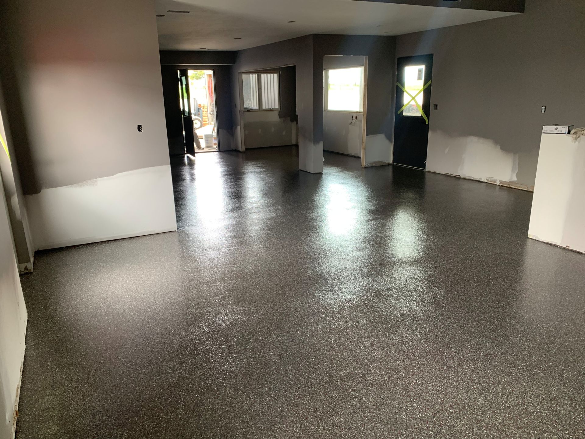 Empty carpeted room with gray walls, white trim, and sunlight coming through the windows and open doorway