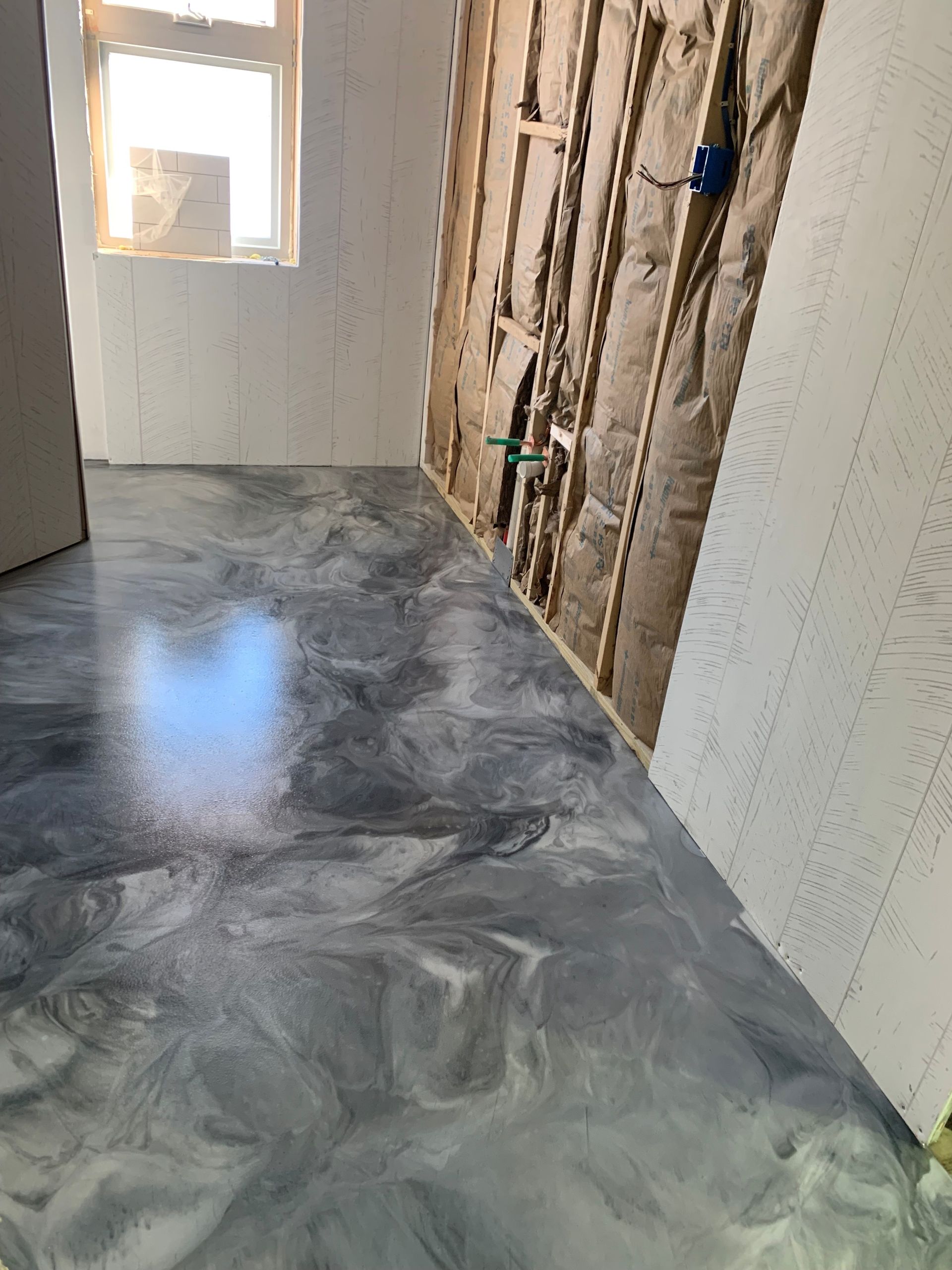 Unfinished room with gray concrete floor, exposed wall framing, and a small window letting in light.