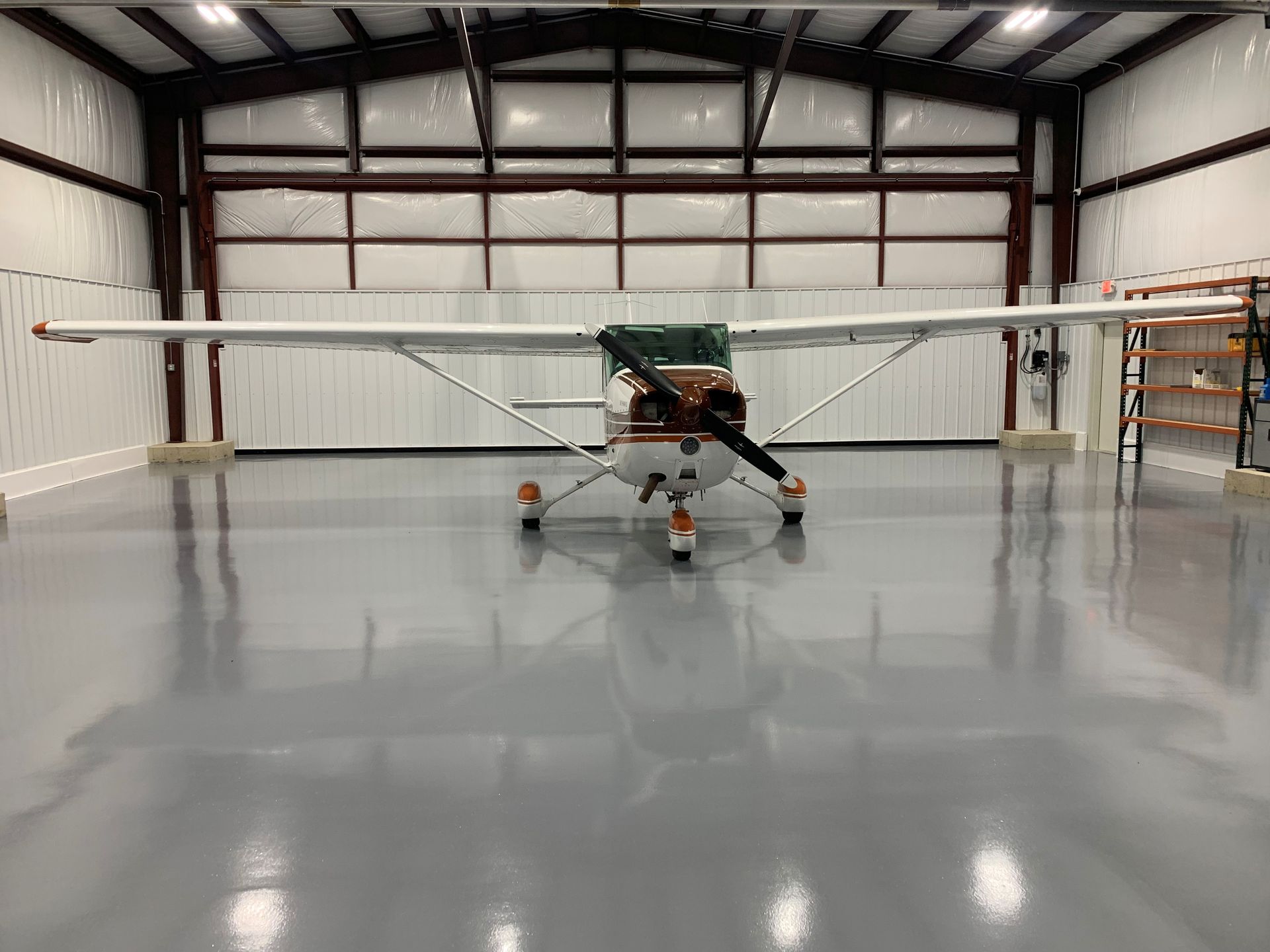 Small airplane parked inside a large hangar with polished concrete floor and open doors.
