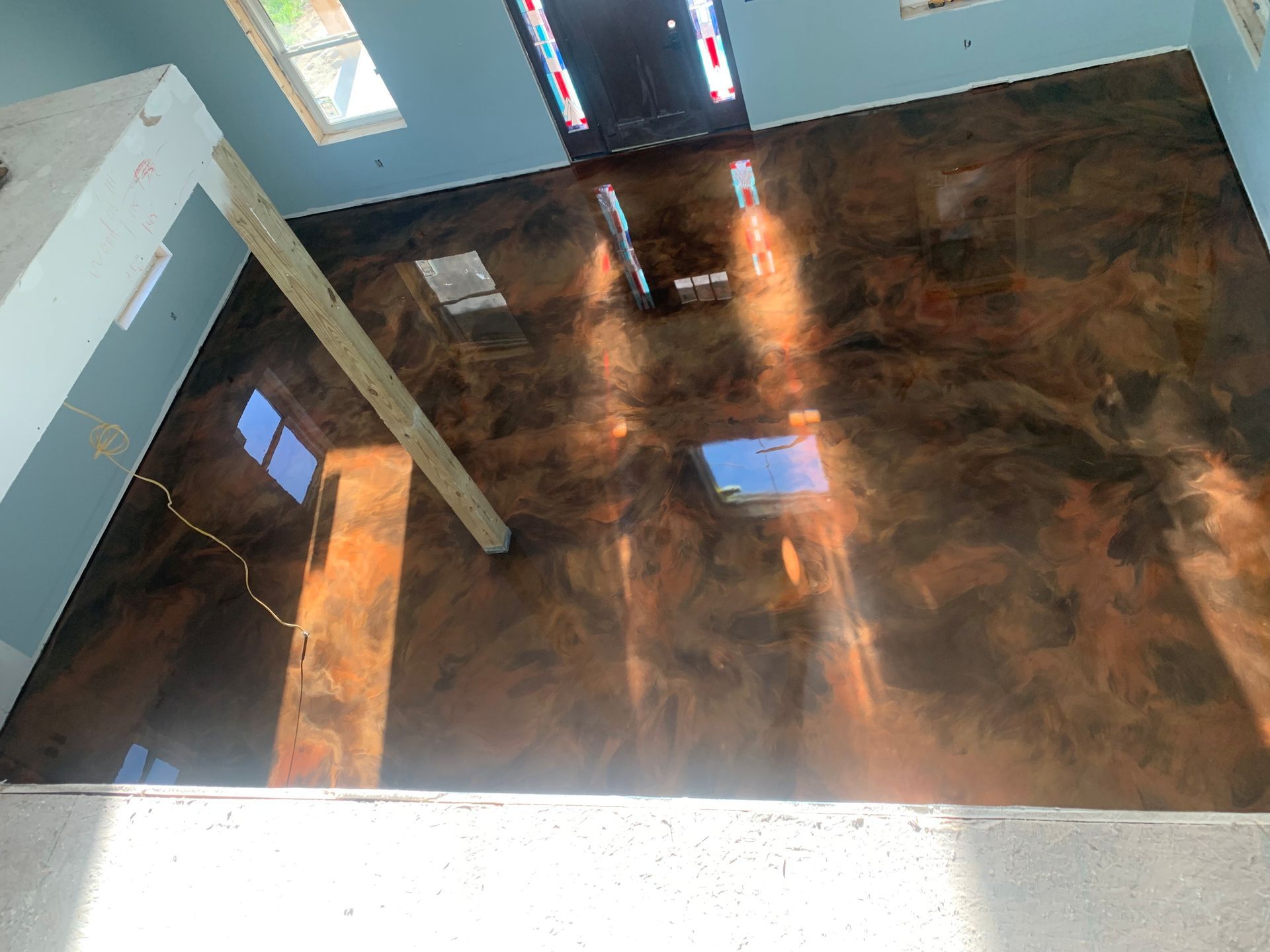 Empty room with glossy dark floor and sunlight streaming through windows.