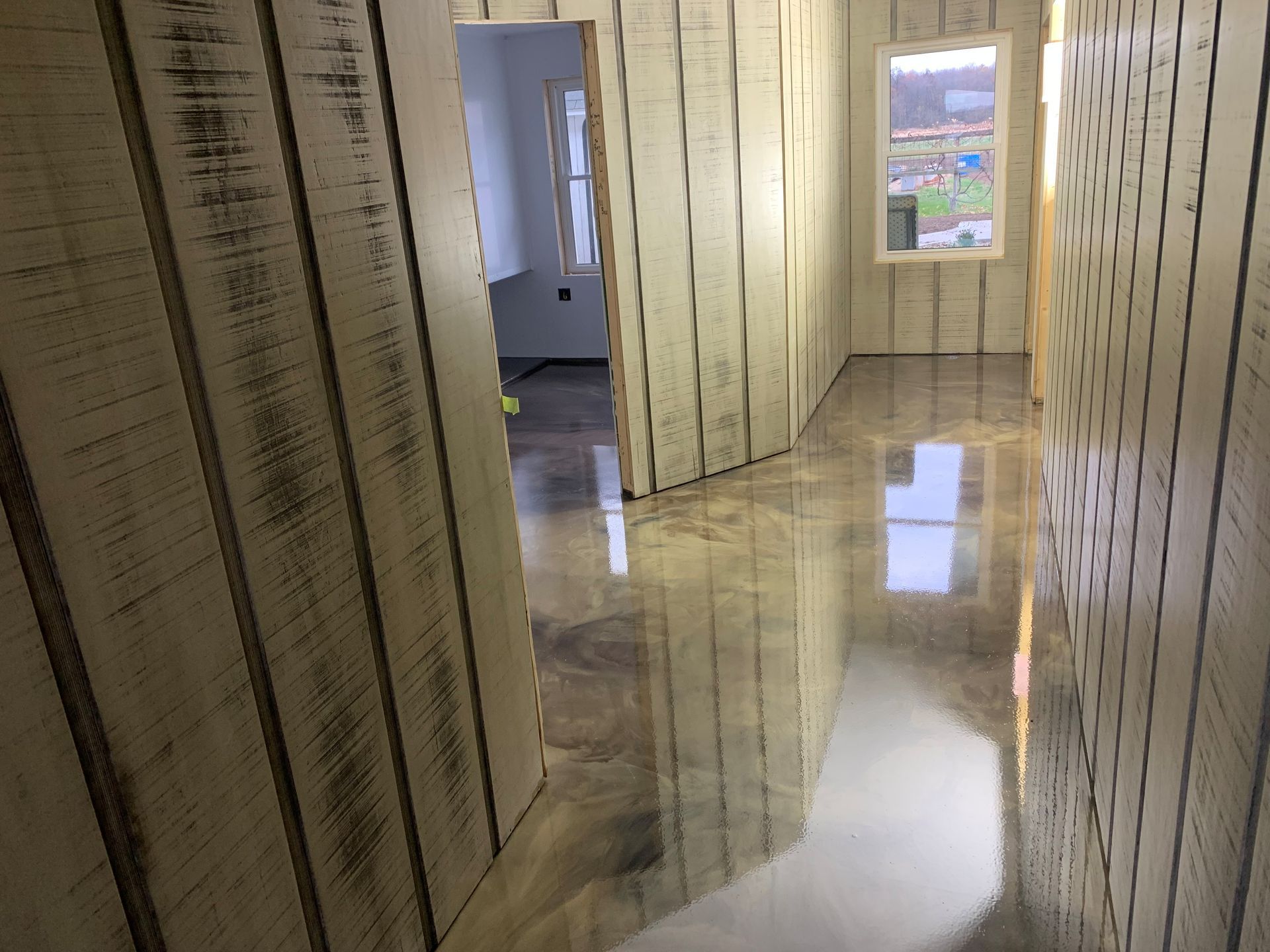 Empty hallway with striped walls, glossy tiled floor, and windows letting in daylight.