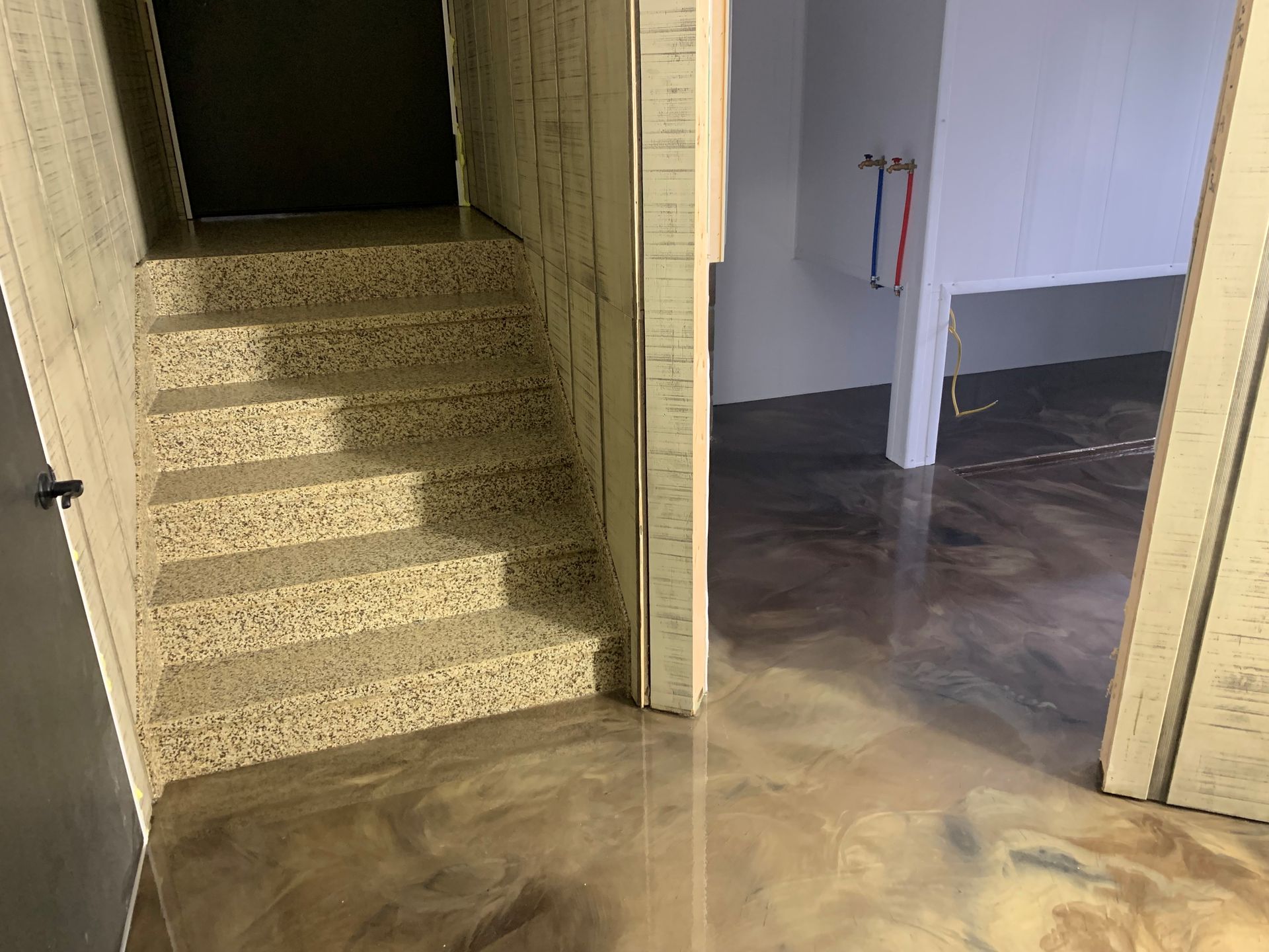 Empty interior hallway with stairs on the left, doorway to a room on the right, and polished concrete floor.