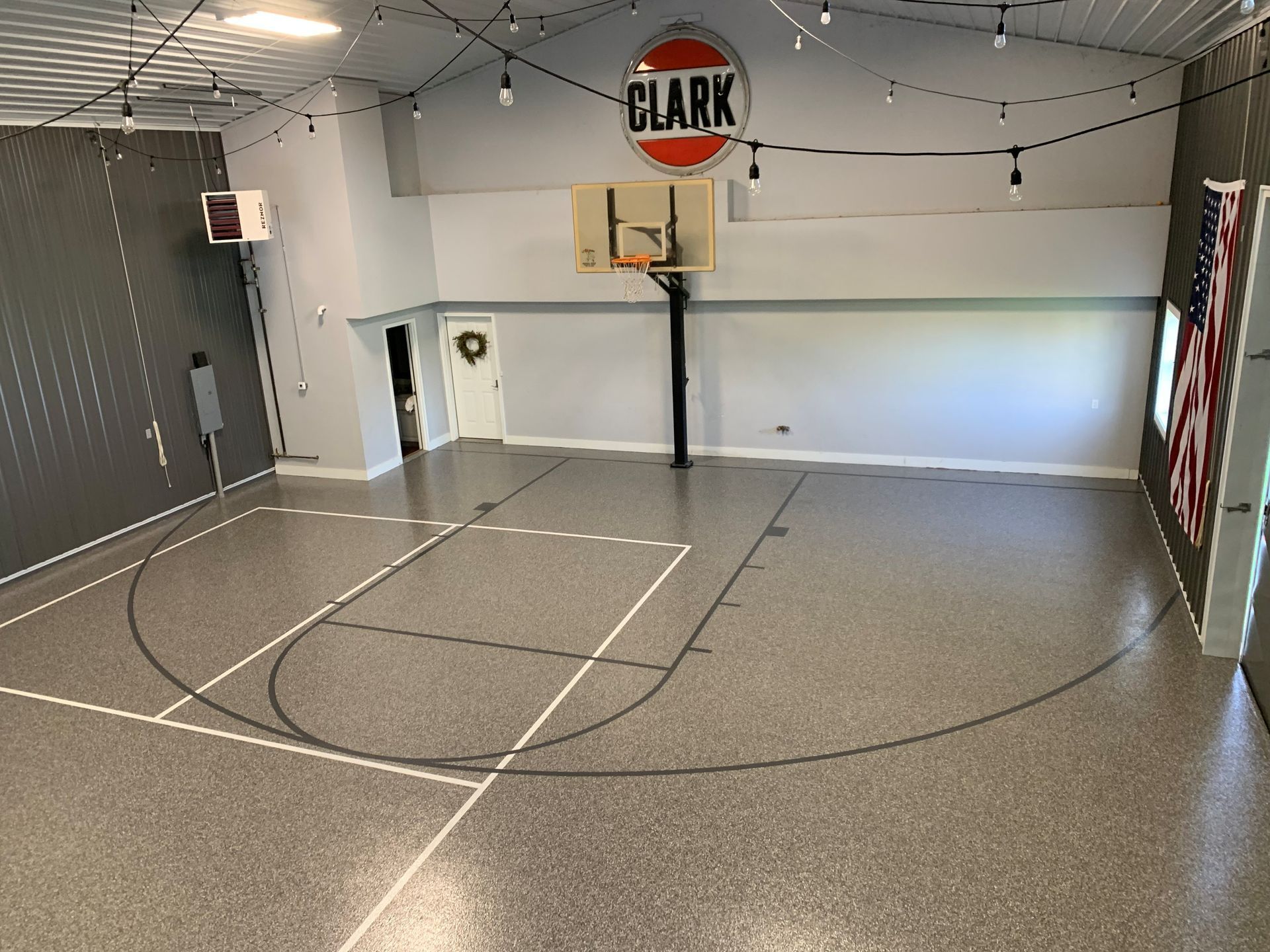 Indoor basketball half-court with gray speckled floor, hoop, and “CLARK” sign on the far wall