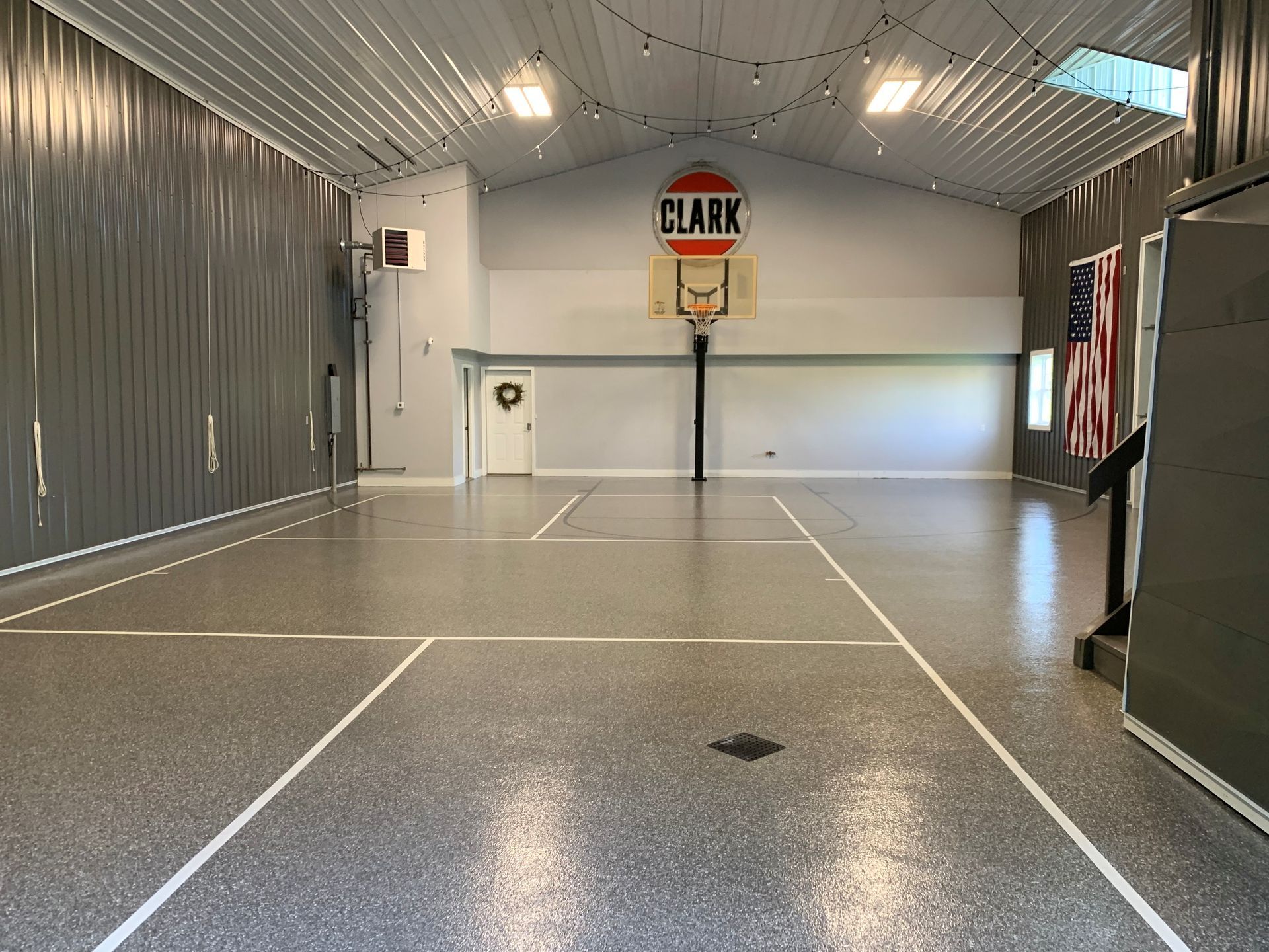 Indoor basketball court with gray walls, speckled floor, hoop, and American flag.