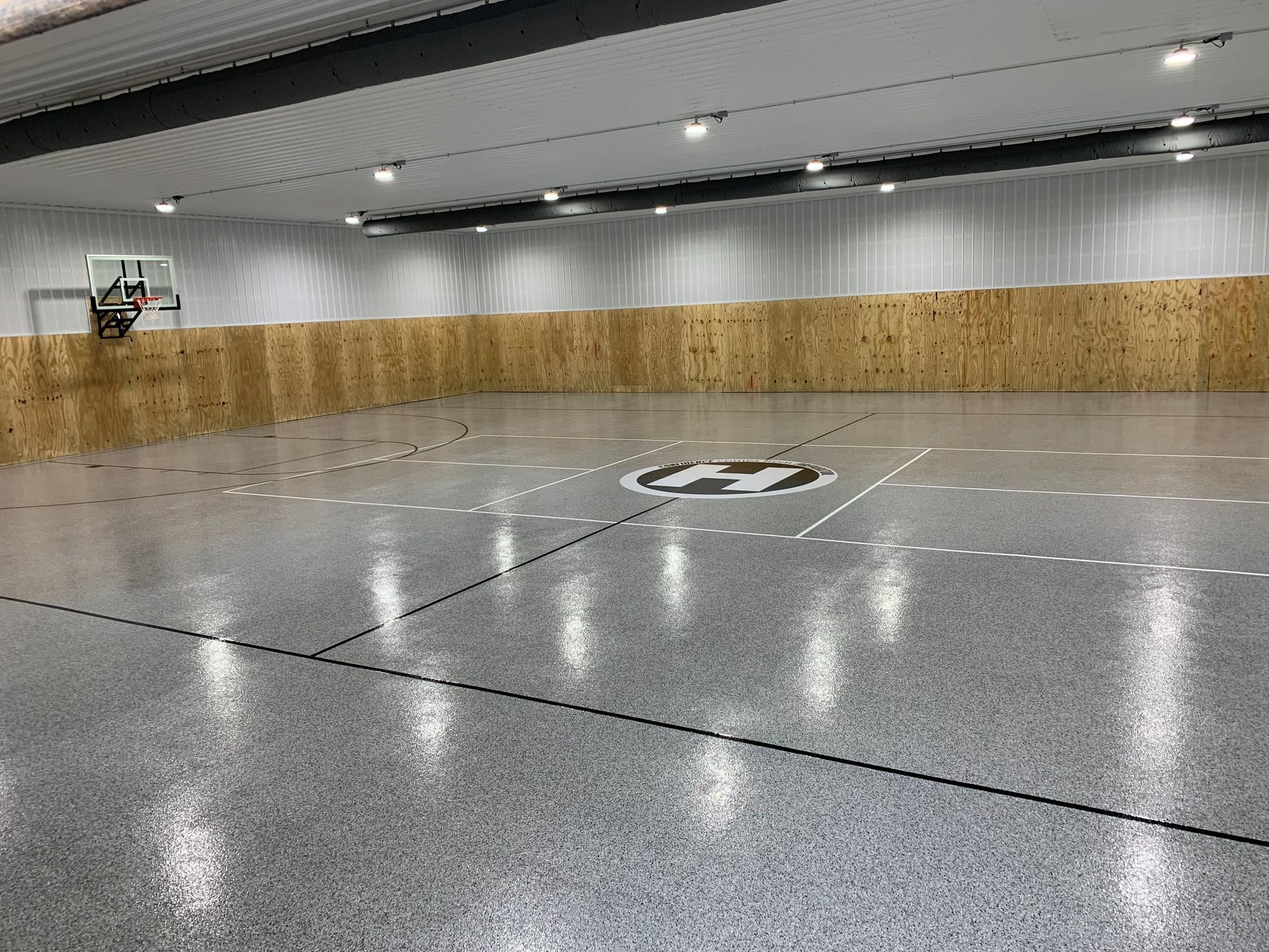 Indoor basketball gym with a glossy court, center logo, and wood-paneled walls underneath bright ceiling lights