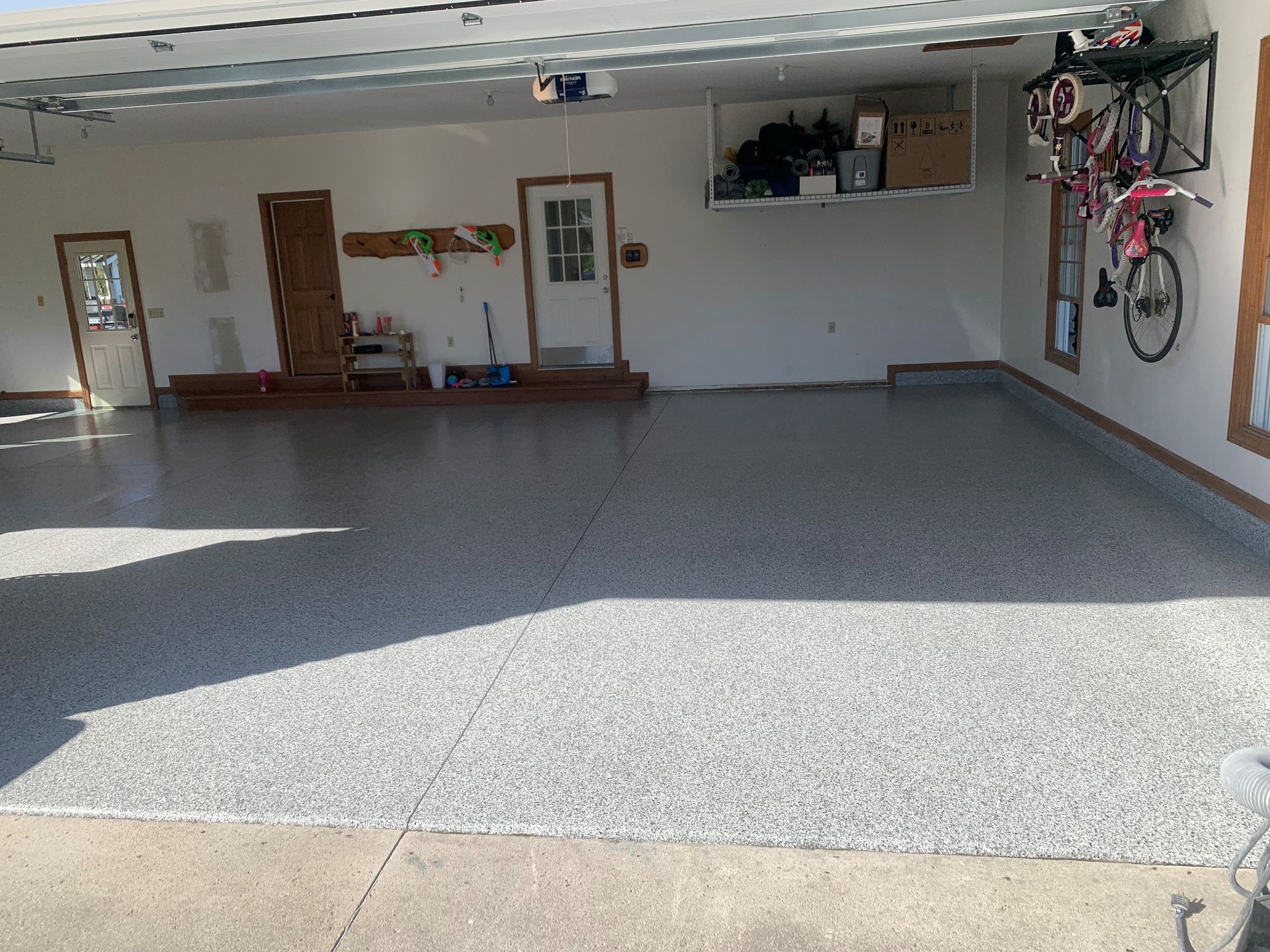 Open garage with gray floor, shelves, bench, and two bicycles on the right wall.