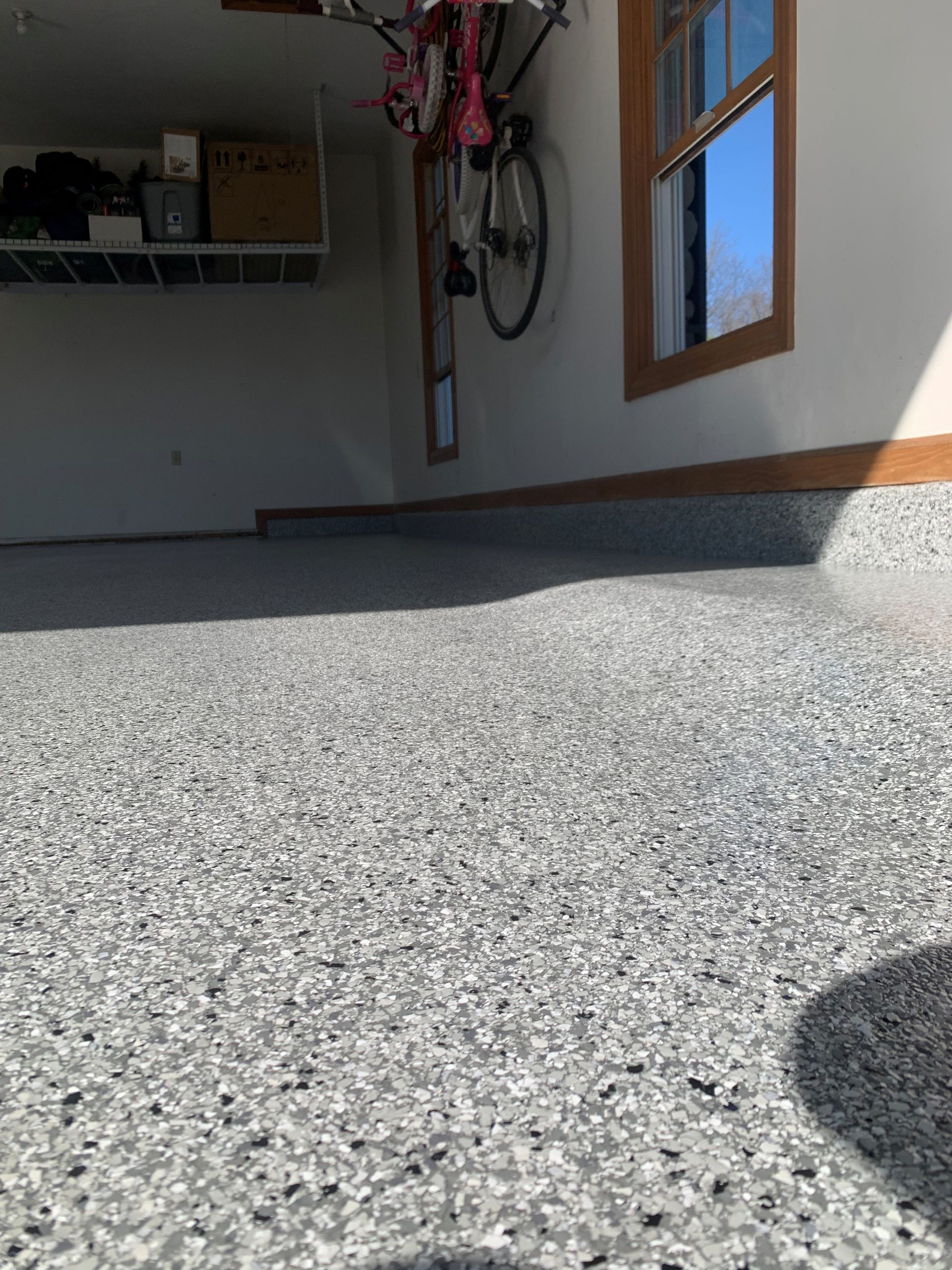 Sunlit garage interior with speckled floor, white walls, hanging bicycles, and a side window.