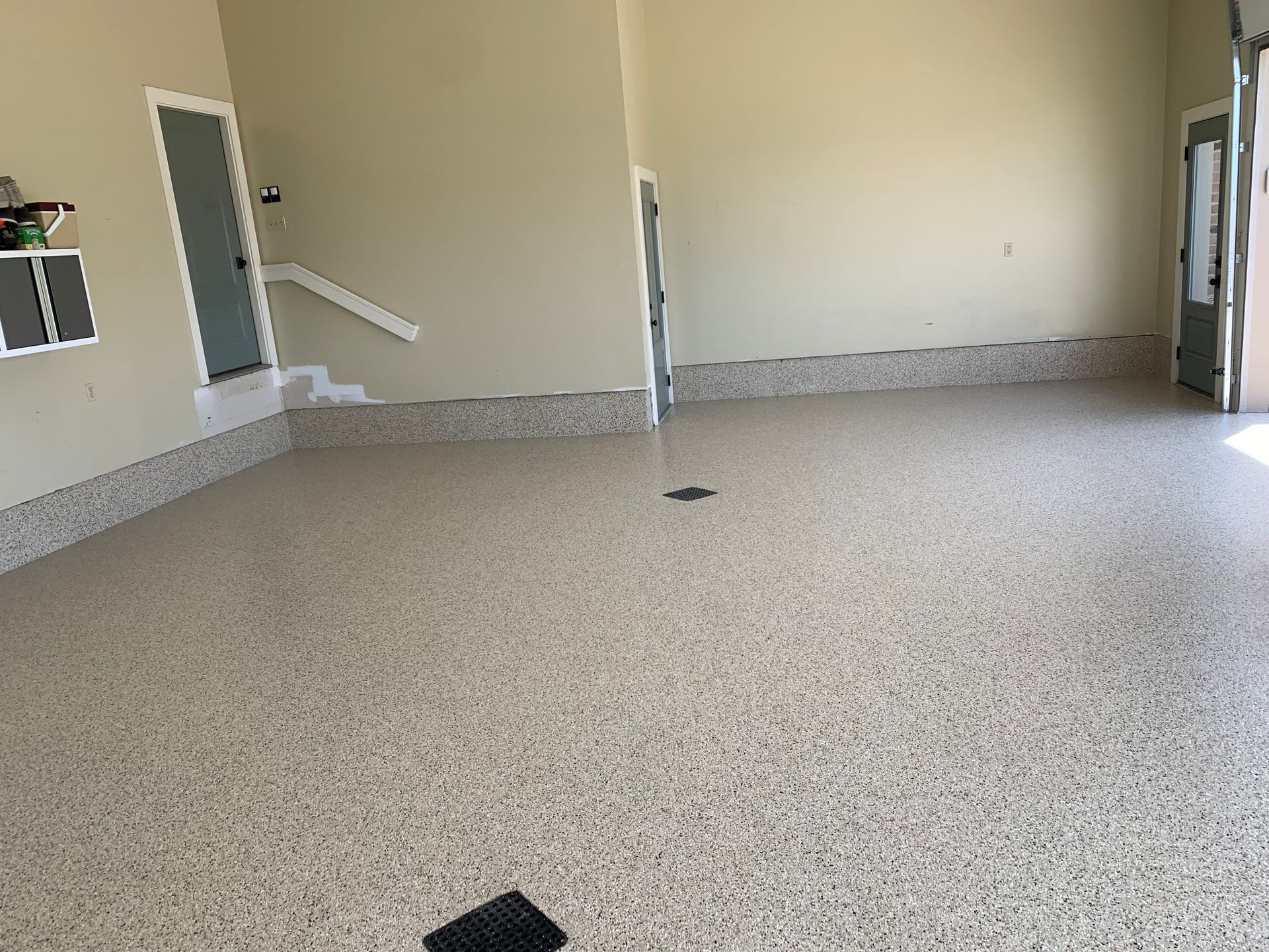 Empty beige room with speckled floor, wall-mounted white handrails, and open doorways
