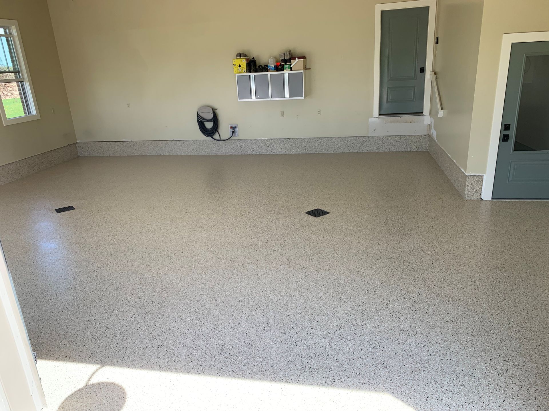 Empty speckled garage floor with walls, a shelf, and doors in the background