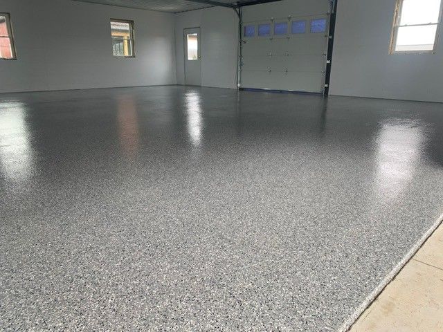 Empty gray garage with a speckled epoxy floor and closed garage door.