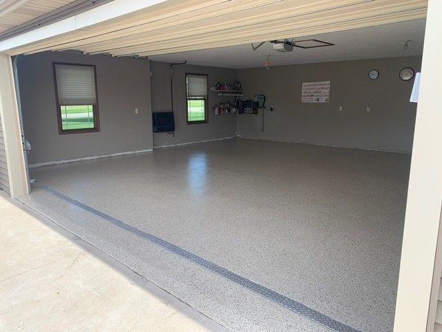 Empty garage with speckled epoxy floor, open door, and a small utility area with windows.