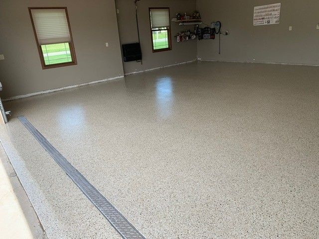 Empty garage with speckled floor, windows, and a wall-mounted utility area.