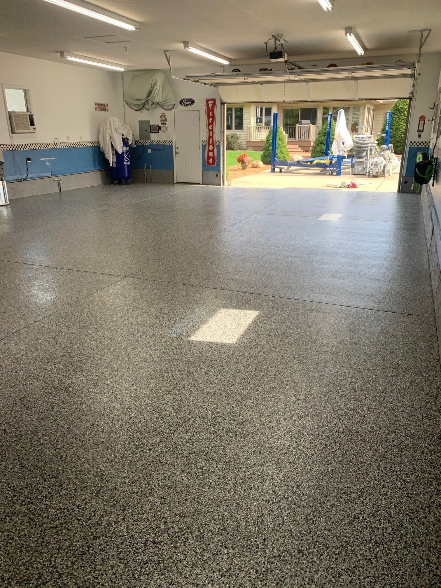 Empty garage with speckled floor, wall cabinets, and an open doorway to a sunny backyard.