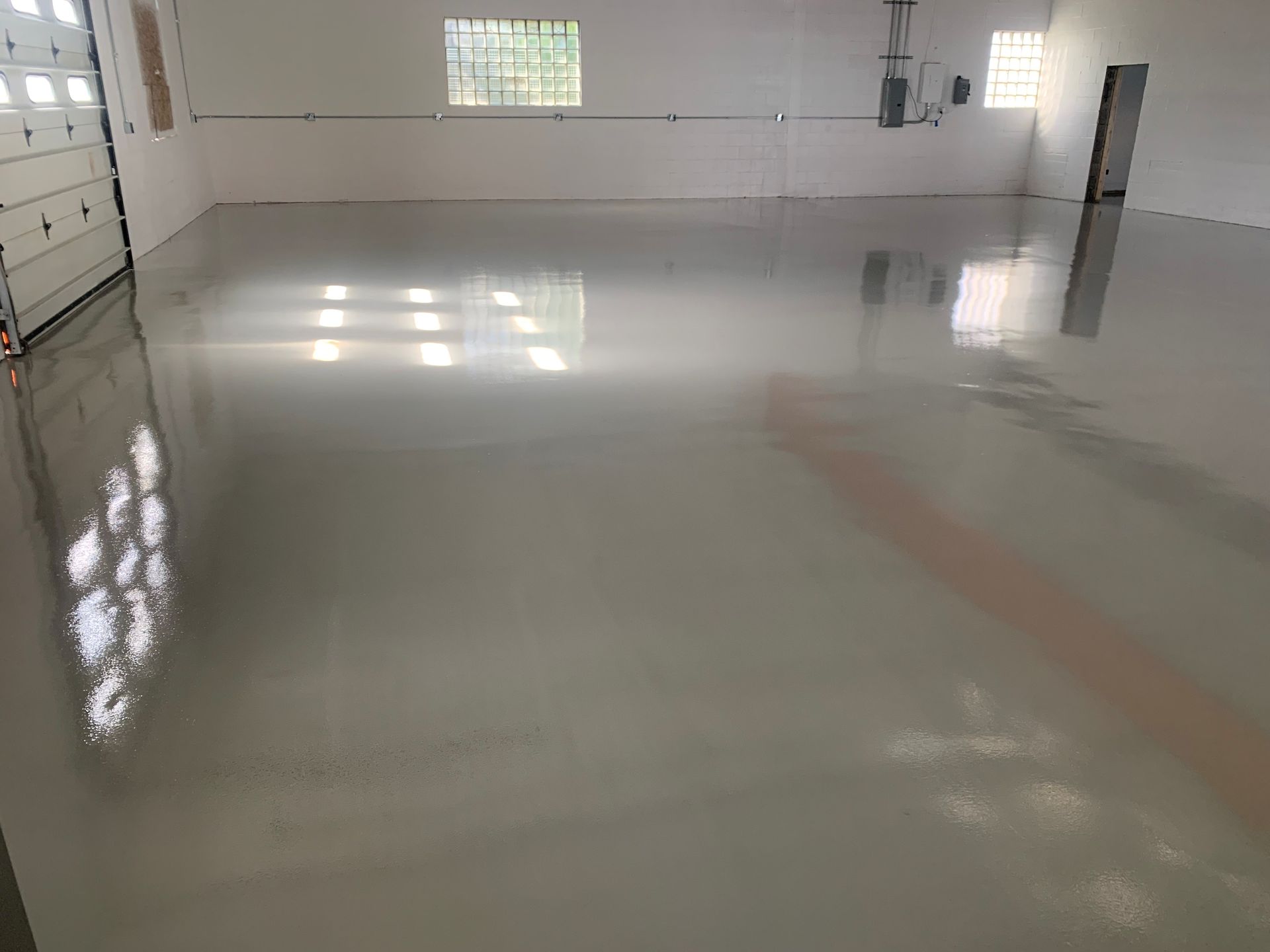 Empty garage with a glossy white epoxy floor and daylight coming through windows.