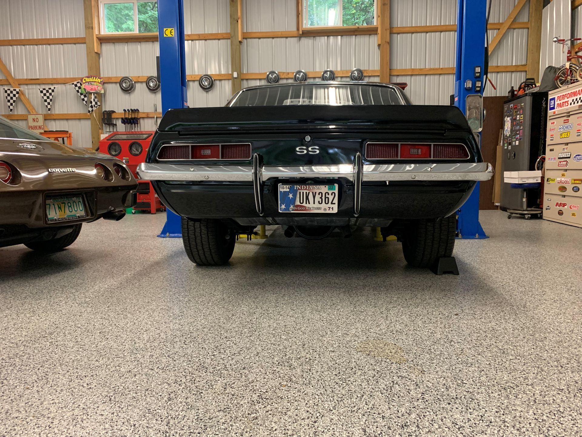 Rear view of a black classic muscle car in a garage, with a brown vintage car beside it.