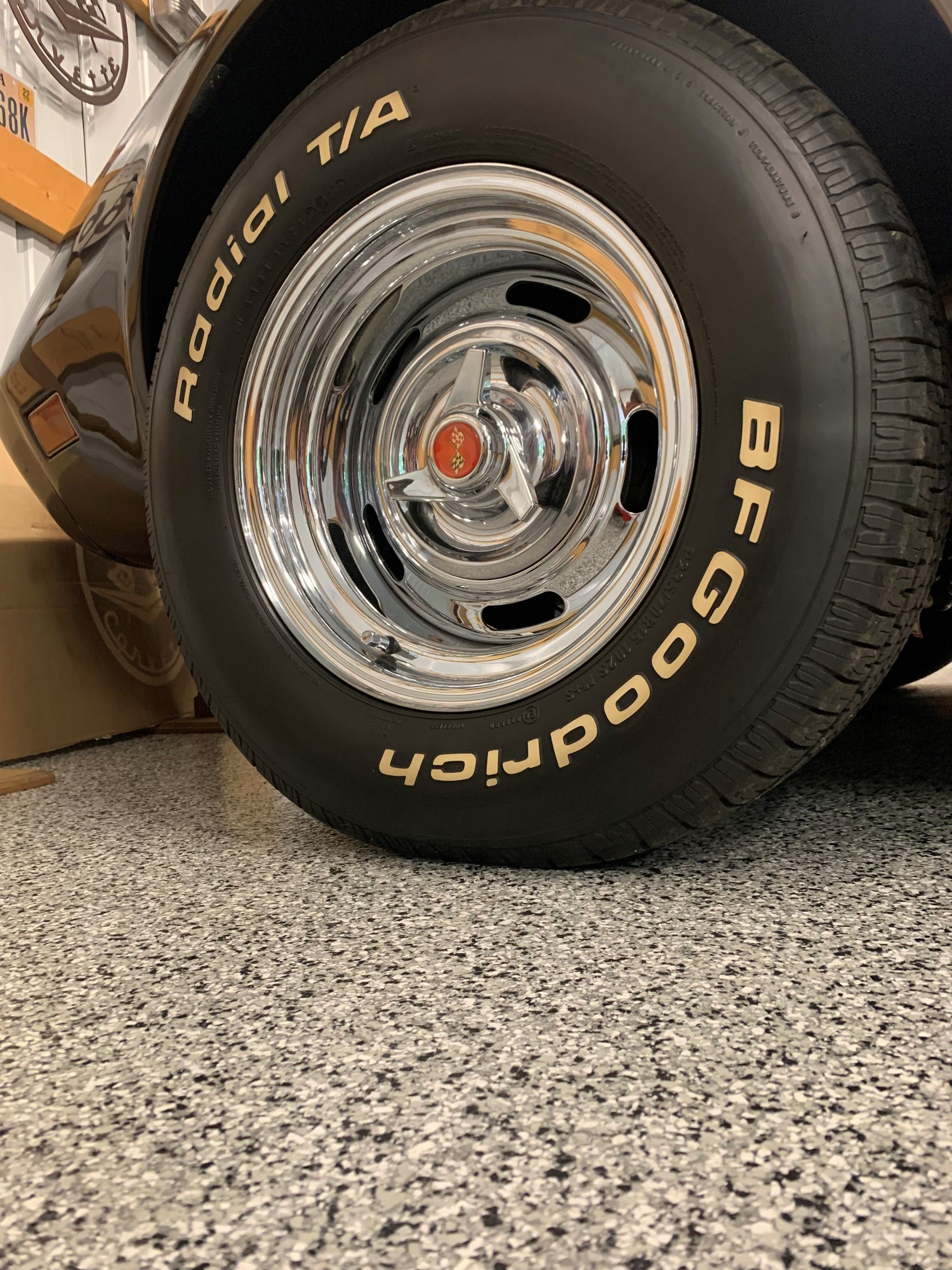 Close-up of a chrome wheel with BFGoodrich tire leaning against a wall on a speckled floor