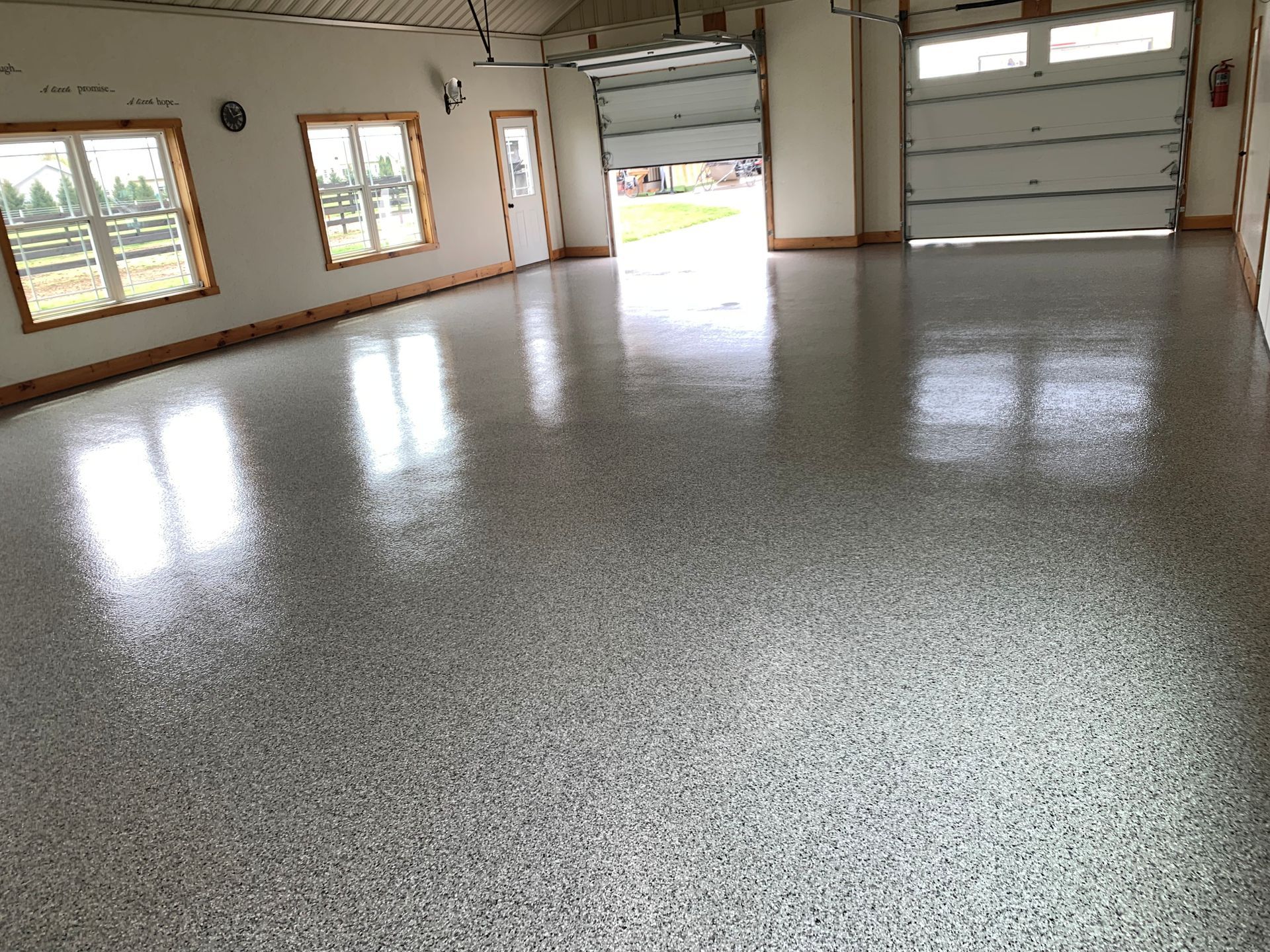 Empty garage with speckled epoxy floor, windows, and an open garage door letting in daylight