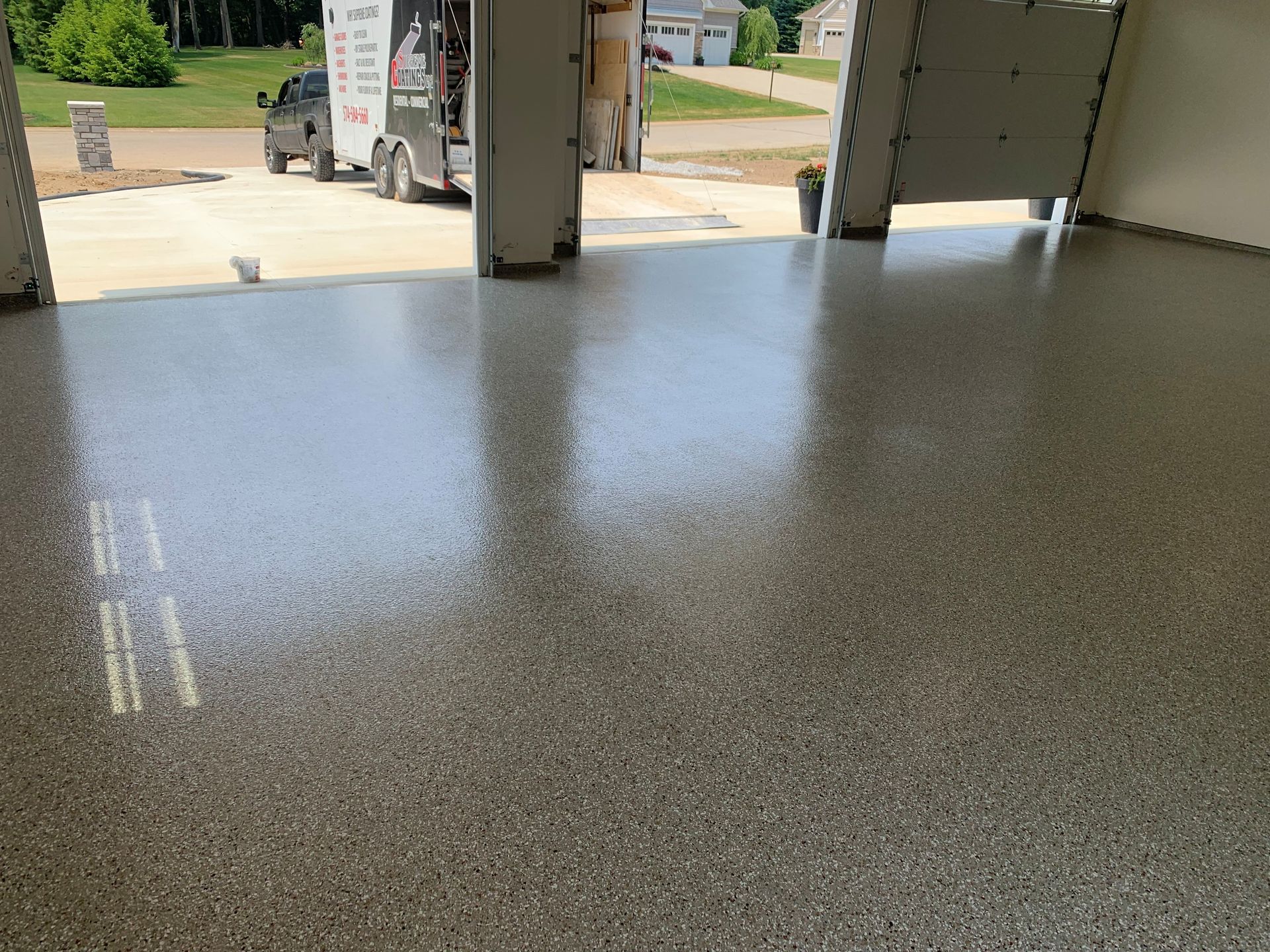 Polished speckled garage floor with open doors looking out to a driveway and lawn
