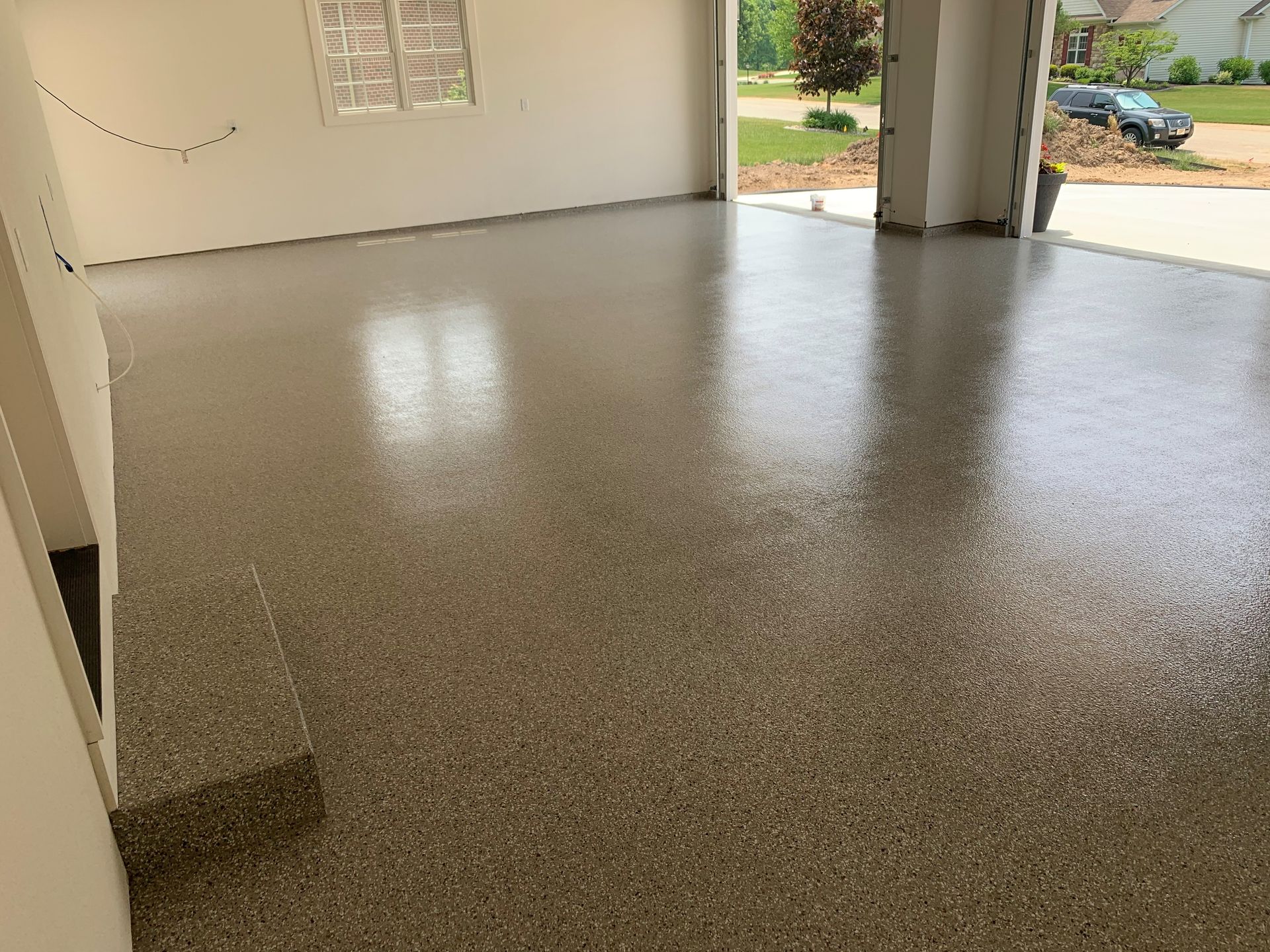 Empty garage with a speckled epoxy floor and open doors to the driveway and yard.