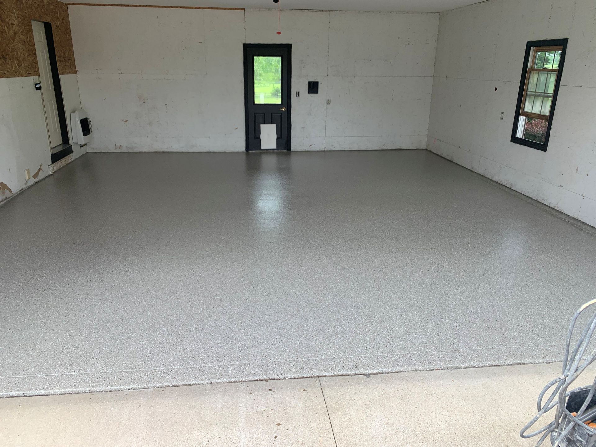 Empty white room with speckled floor, windows on the walls, and a door at the far end