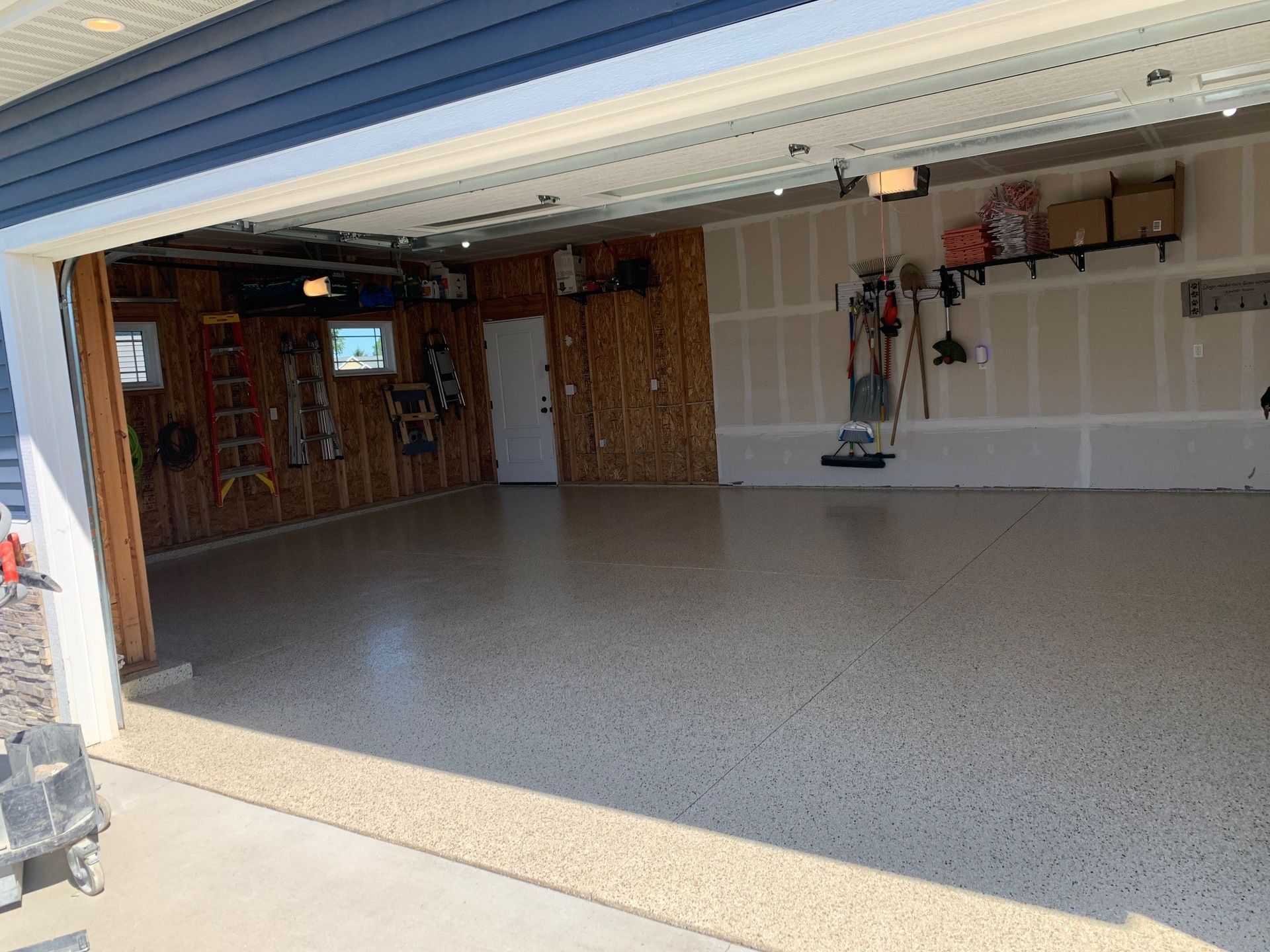Open garage with speckled floor, wood-paneled interior, and shelves along the back wall.