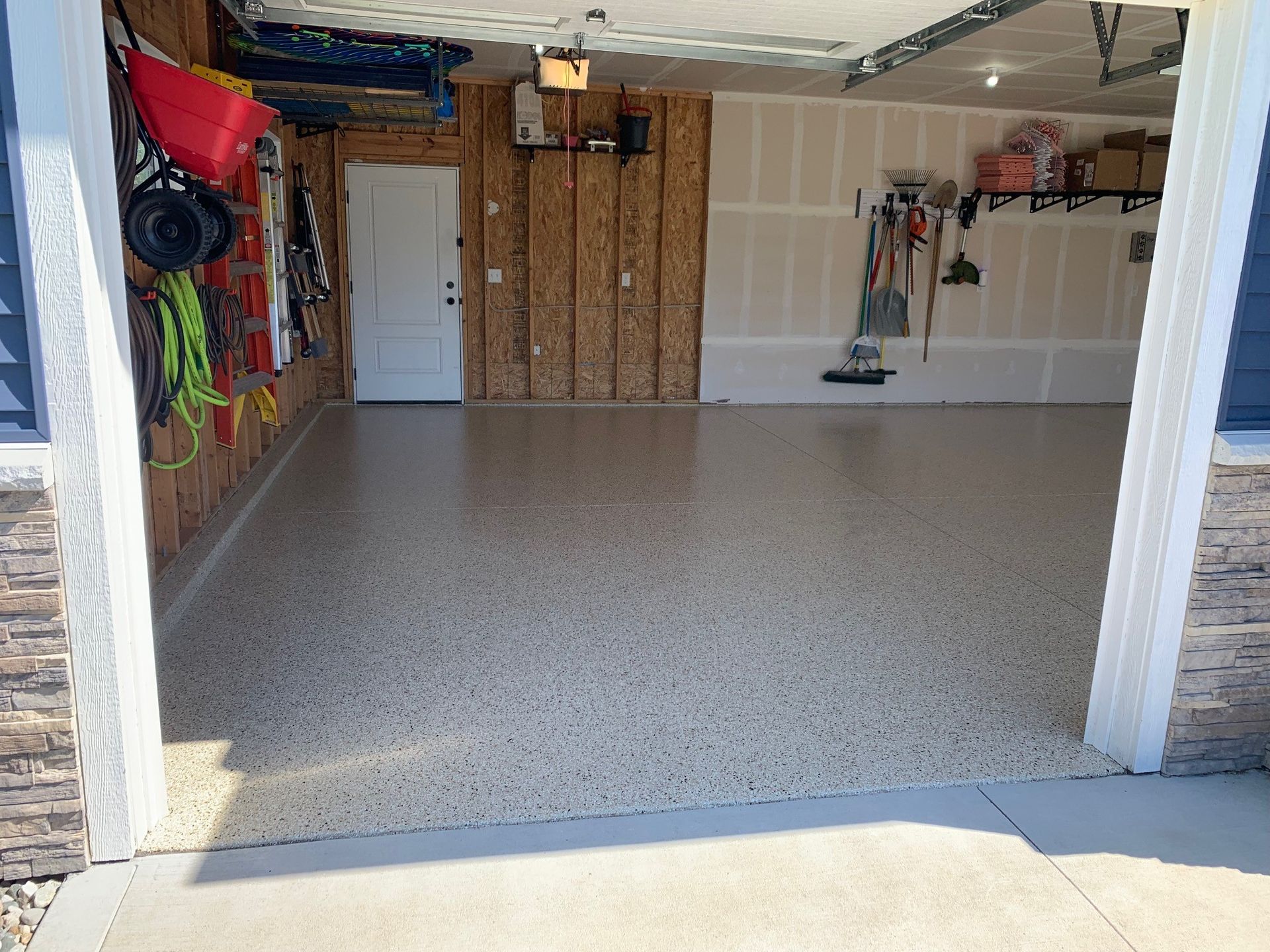 Empty garage with speckled floor, storage on walls, and a white door at the back