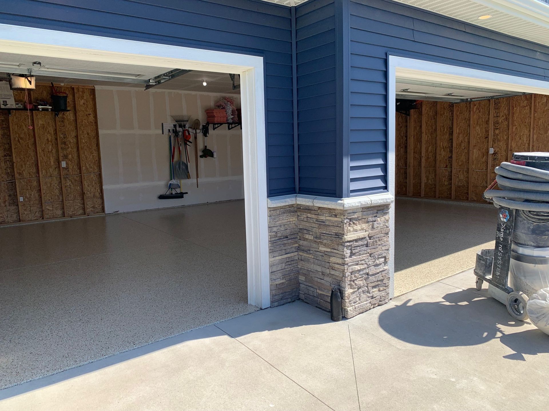 Open garage with blue siding, concrete floor, and a stone column, showing a clean unfinished interior.