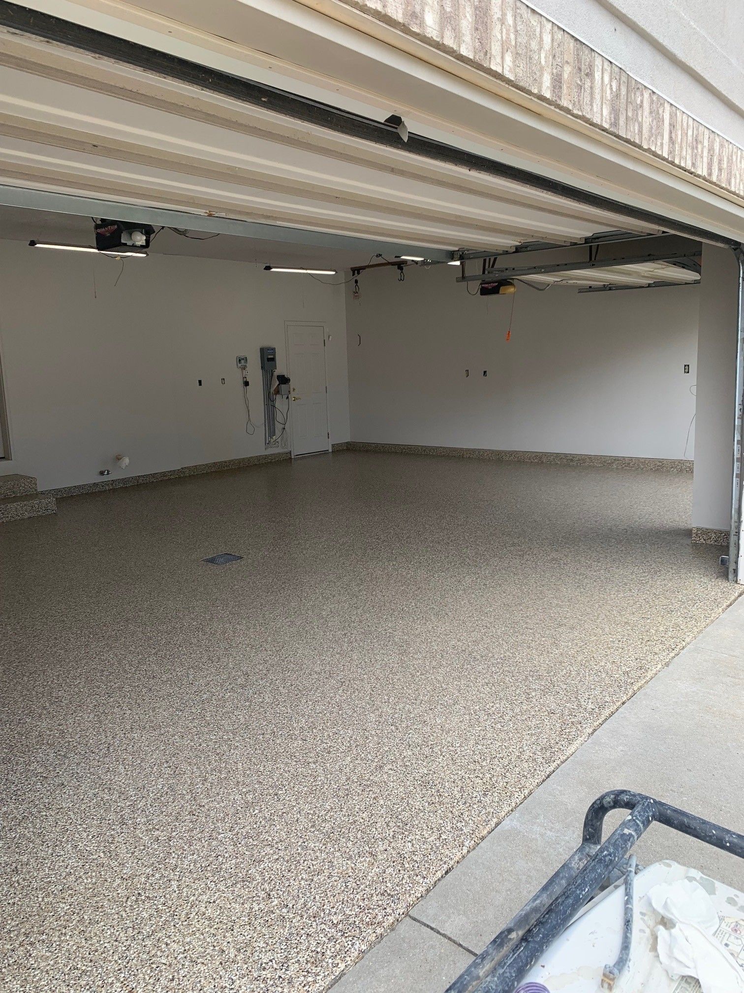 Empty garage with a beige pebble-finish floor and a partially open overhead door