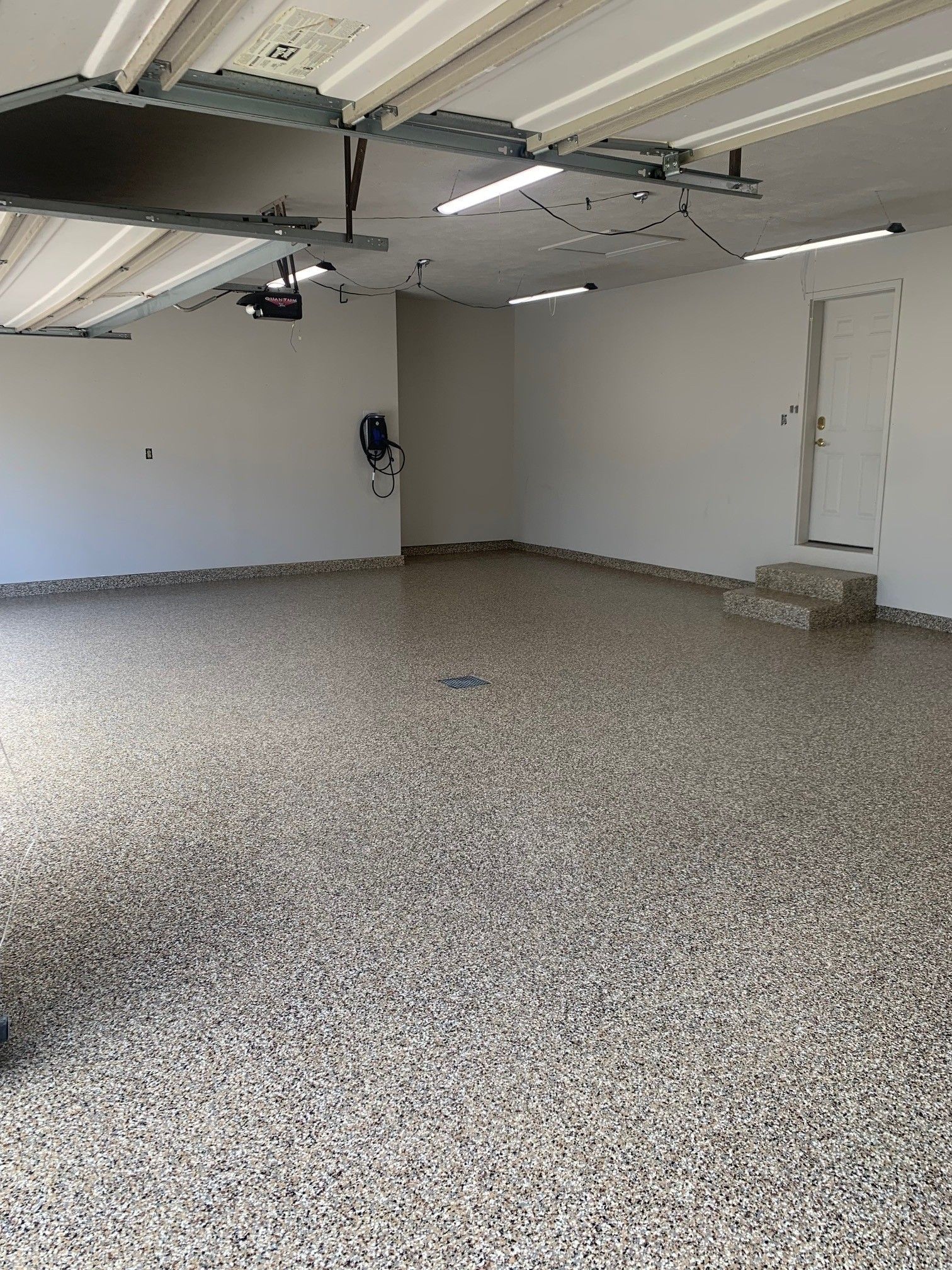 Empty garage interior with speckled floor, white walls, and overhead fluorescent lights