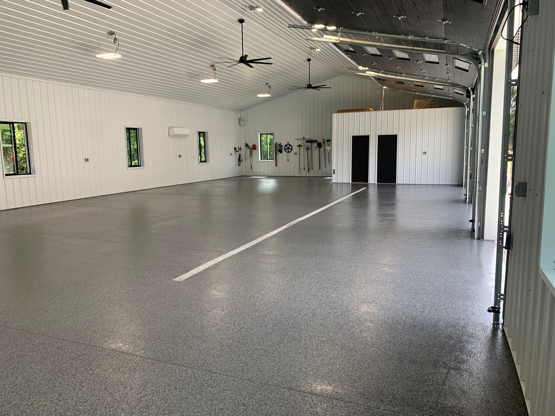 Empty indoor hall with polished gray floor, white walls, ceiling fans, and small windows along the side.
