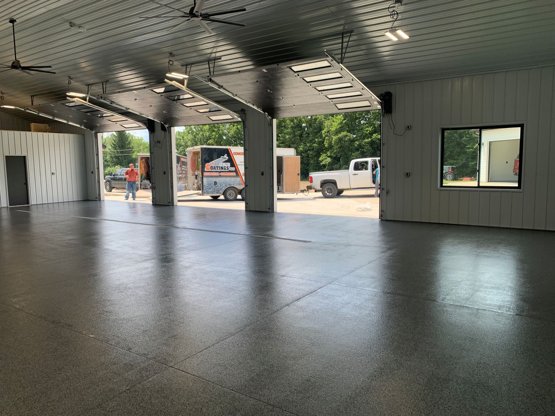 Spacious garage bay with polished floor, open doors, and vehicles parked outside.