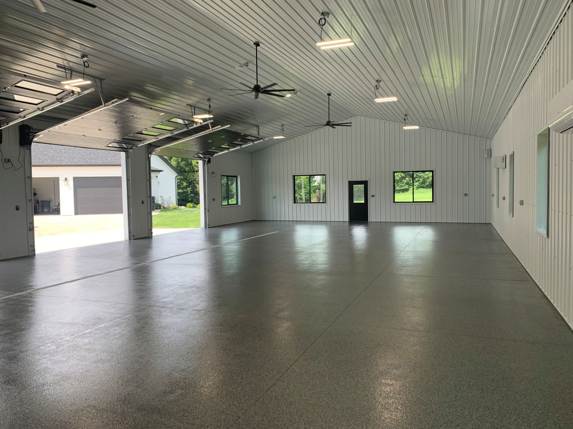 Empty indoor garage with white walls, gray floor, and open bay doors letting in daylight